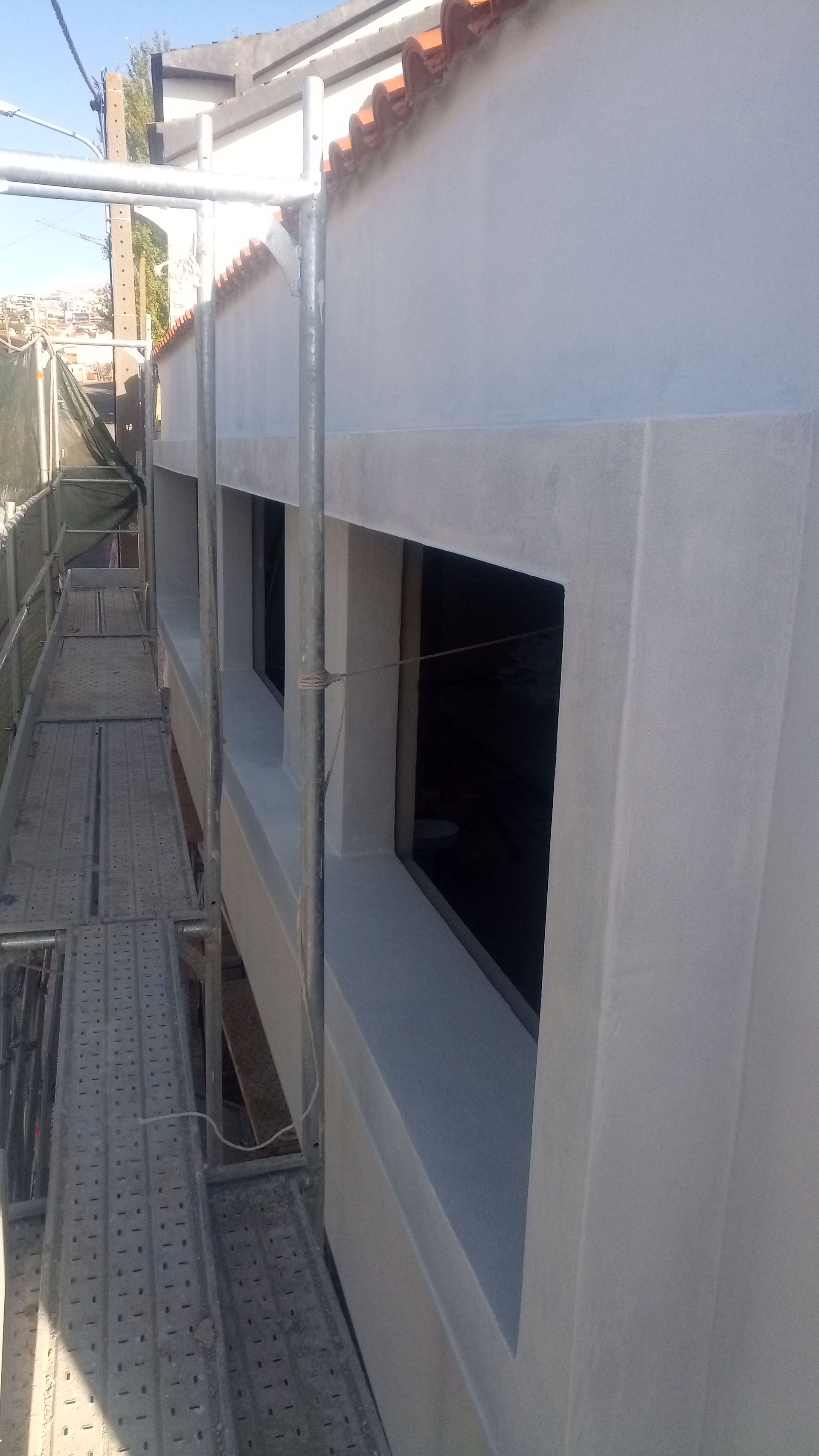 Exterior do edifício com duas janelas escuras e andaimes.