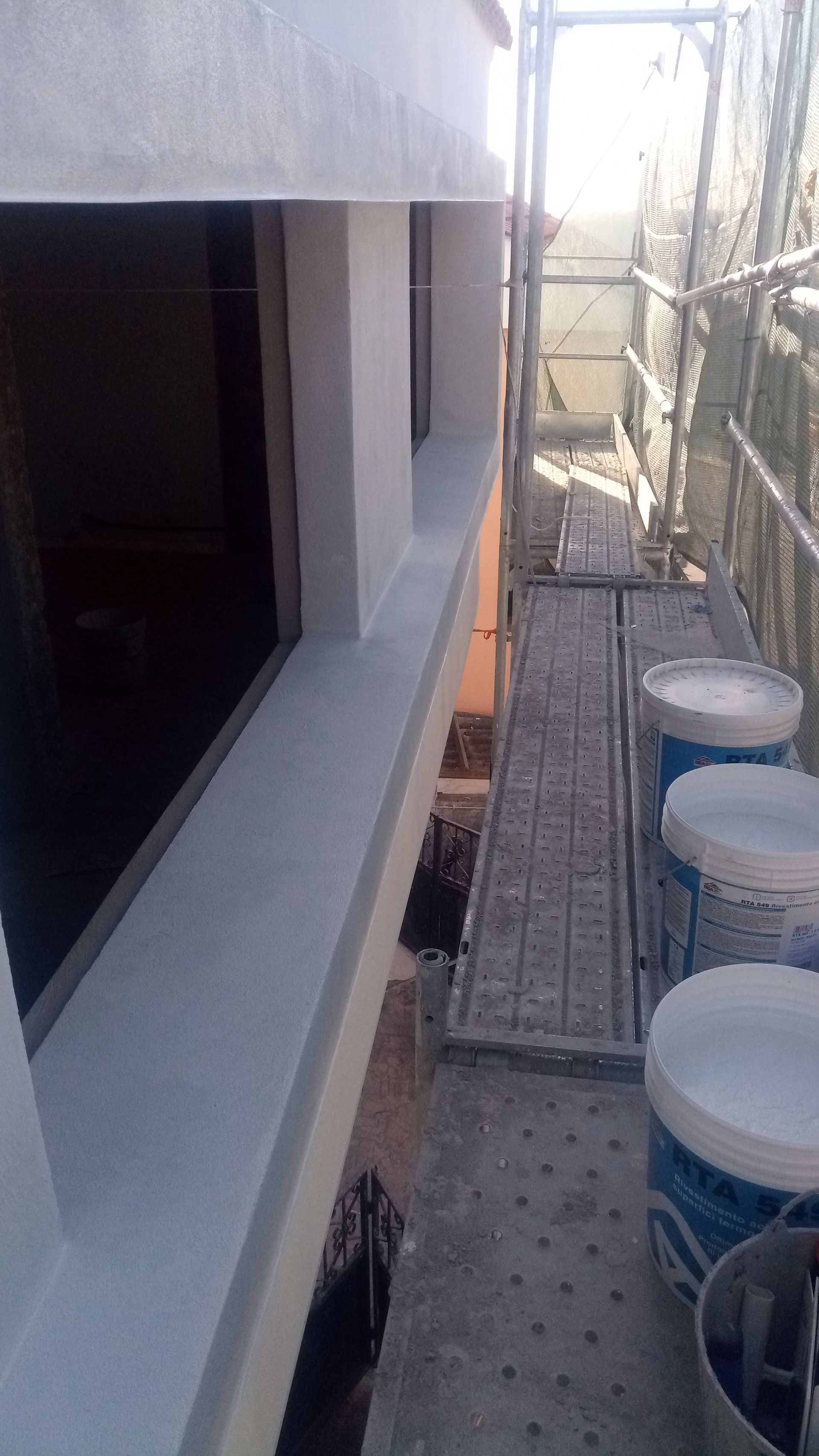 Parede externa com moldura de janela pintada e andaime ao lado. Baldes estão sobre o andaime.