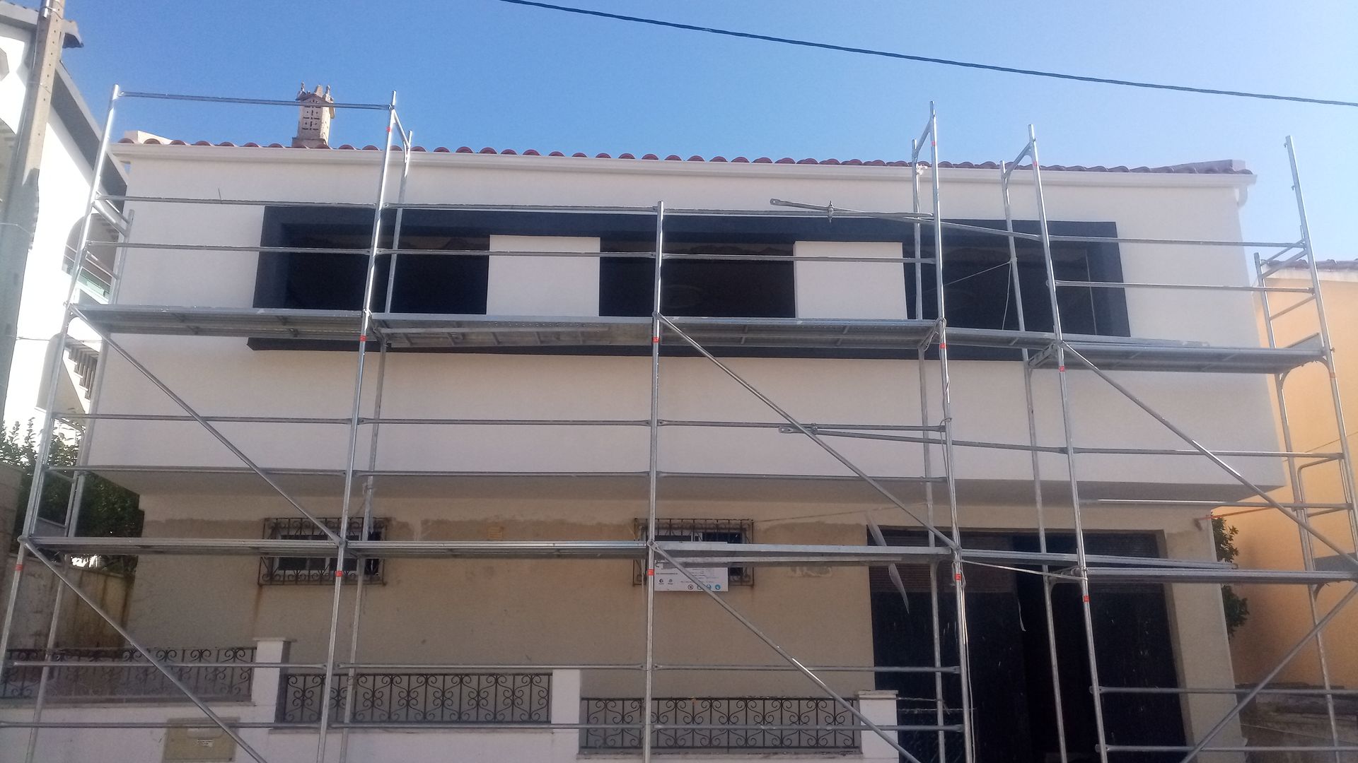 Prédio branco com andaimes, céu azul, janelas com persianas escuras.