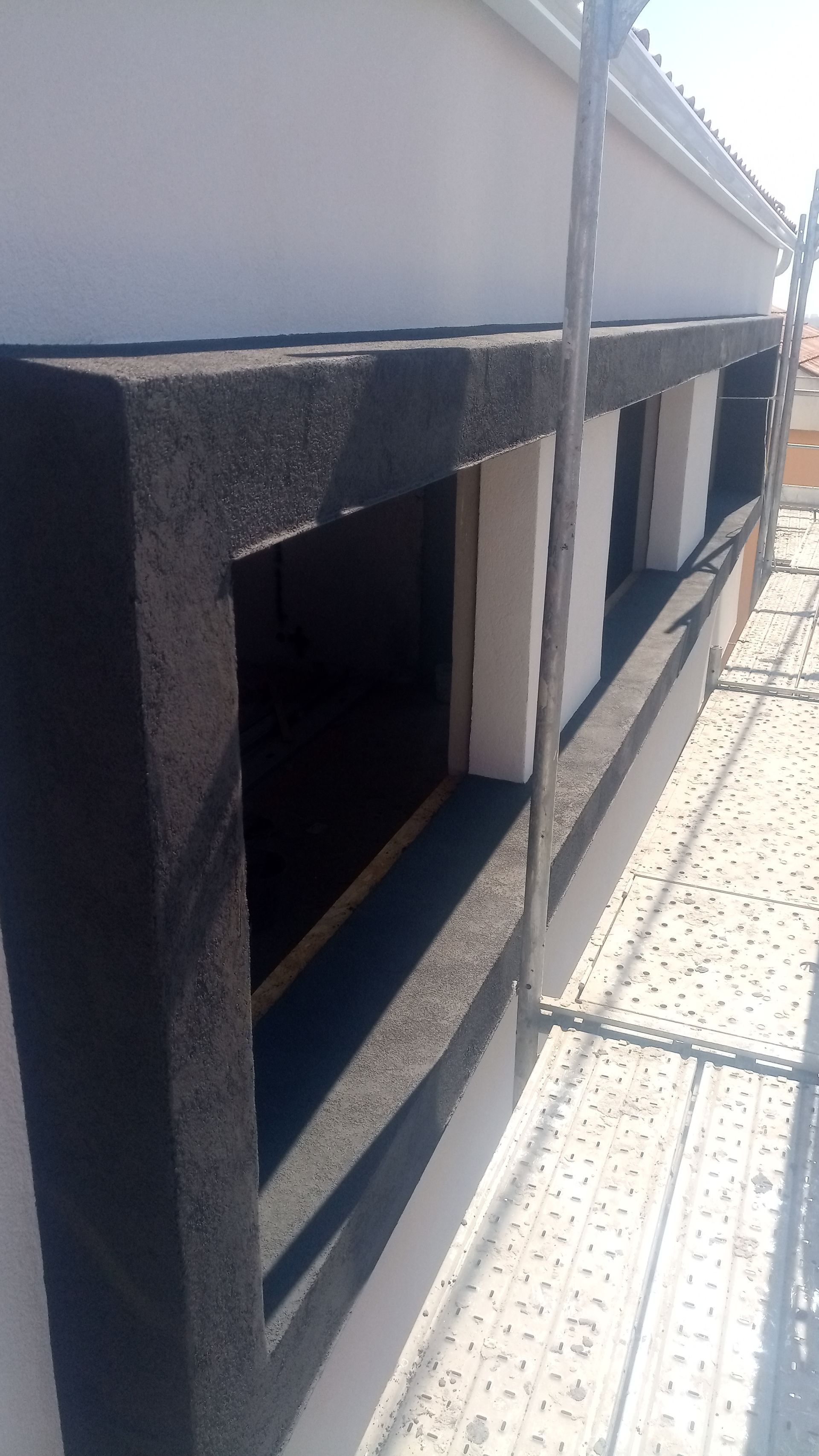 Vista exterior do edifício com caixilhos de janelas escuros e texturizados, e andaimes.