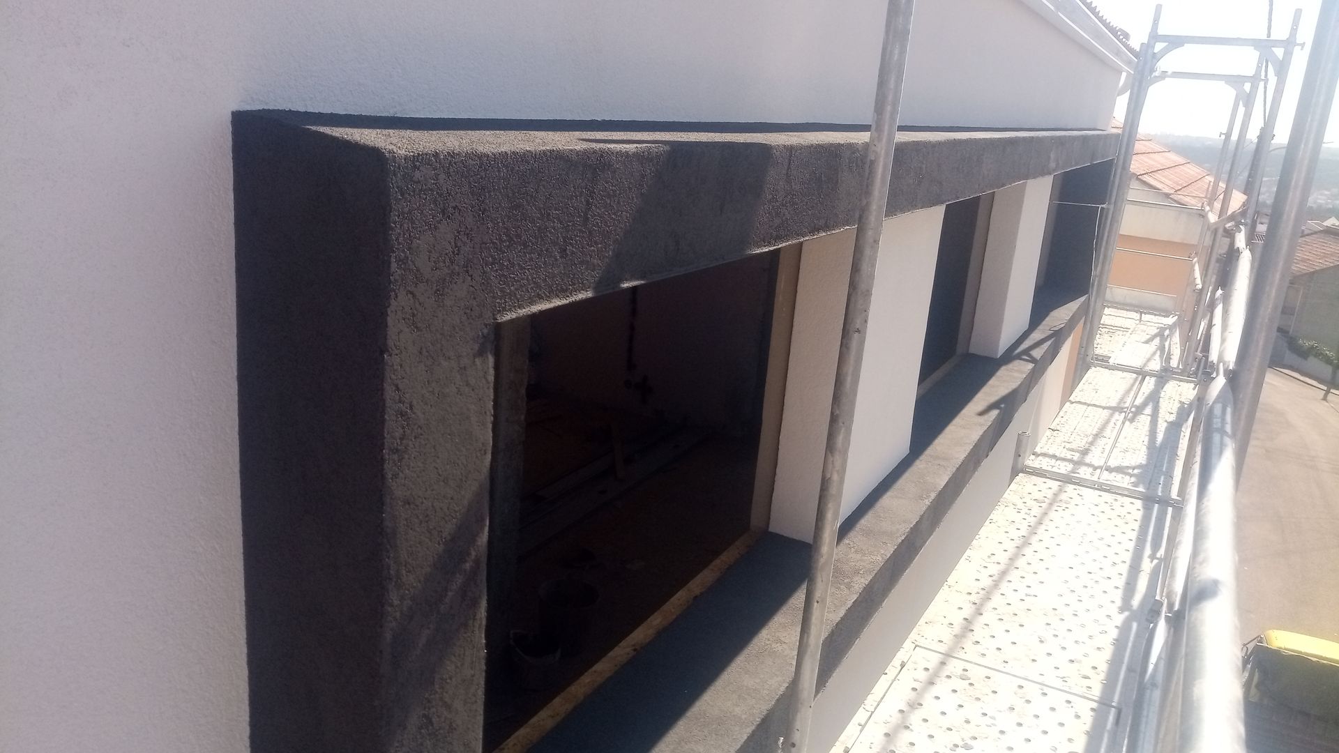 Fachada do prédio com instalação de novas esquadrias. Moldura texturizada preta ao redor das janelas em parede branca.