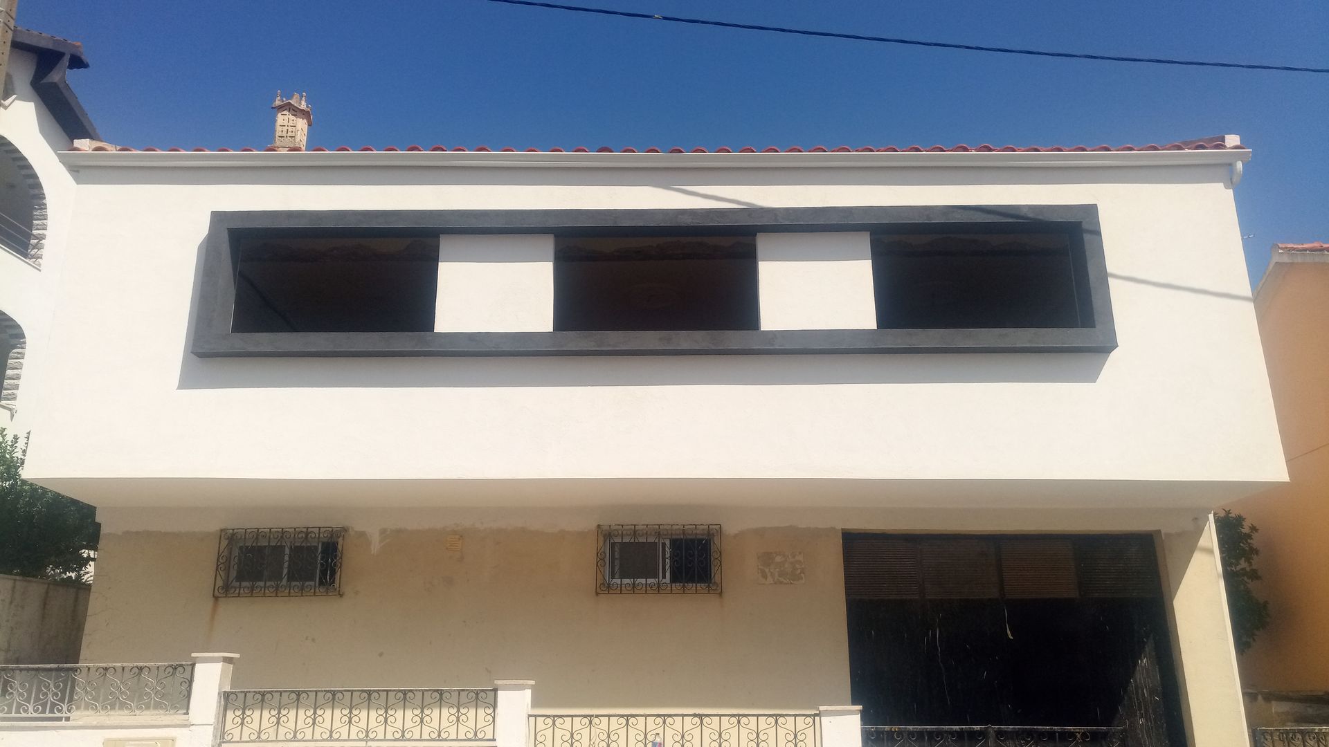 Prédio branco de dois andares com molduras de janelas escuras. Cerca e portão de metal na frente.