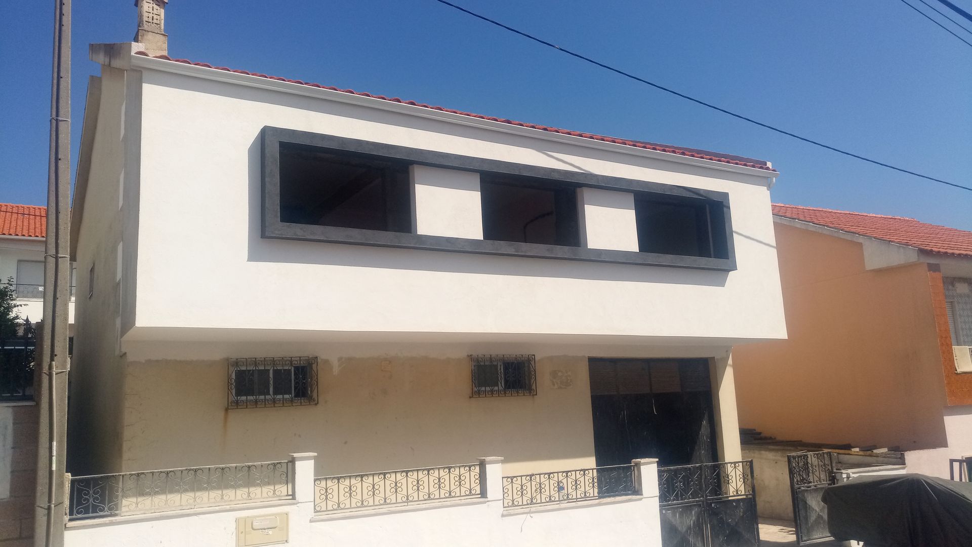 Casa branca de dois andares com molduras de janelas escuras; céu azul ao fundo.