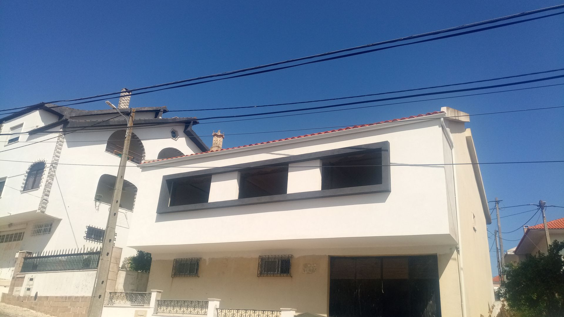 Prédio branco com molduras de janelas escuras sob um céu azul claro. Fios elétricos percorrem o topo.
