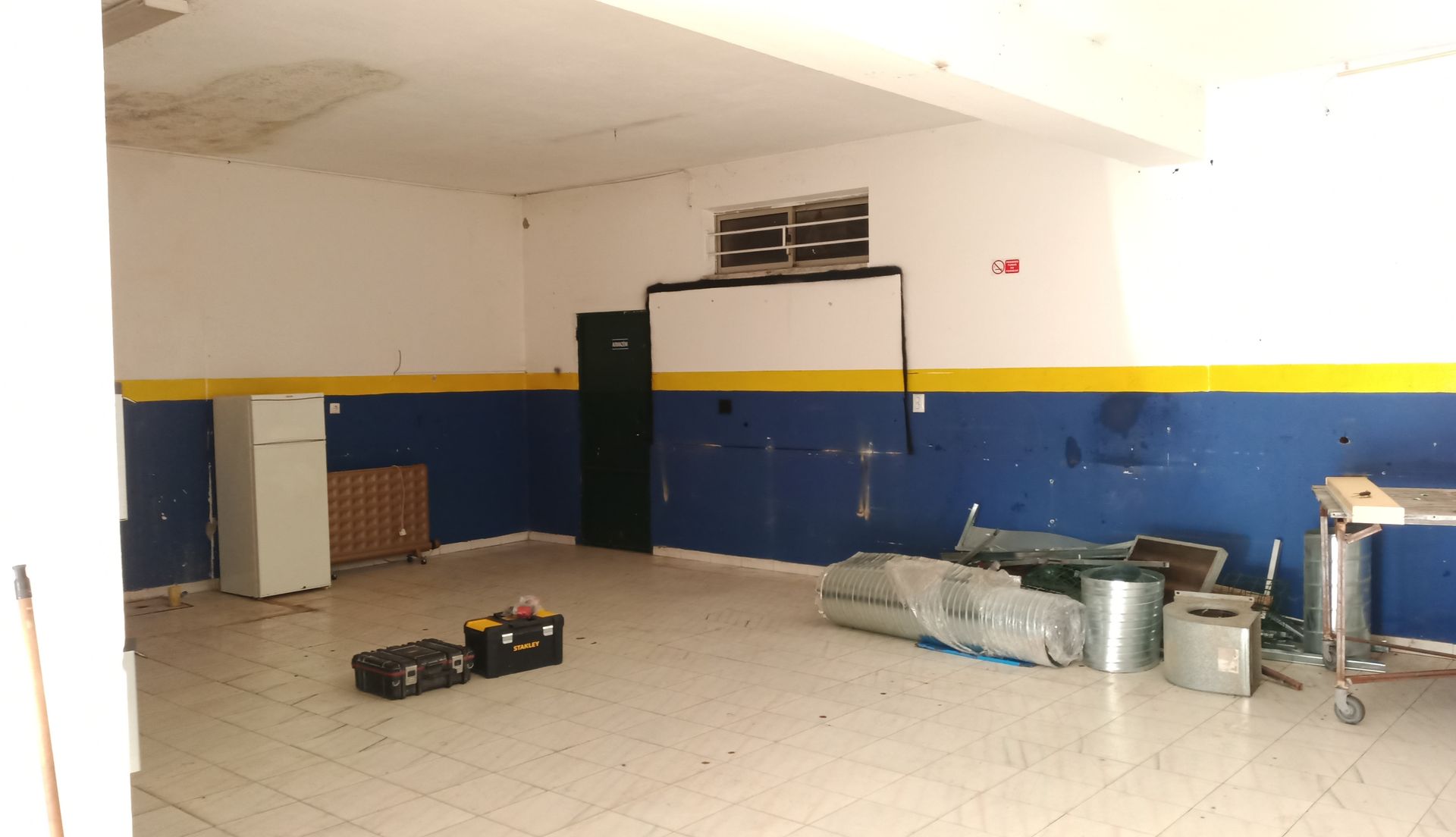 Garagem vazia com paredes brancas, detalhes em azul e amarelo e alguns equipamentos.