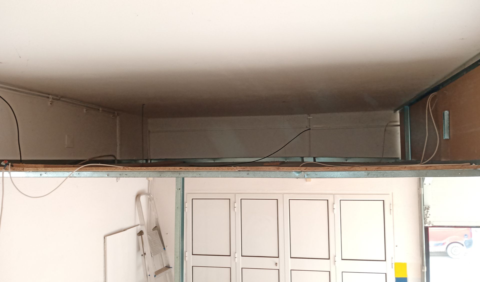 Canteiro de obras interno com teto de gesso acartonado, paredes parcialmente construídas e porta branca fechada.