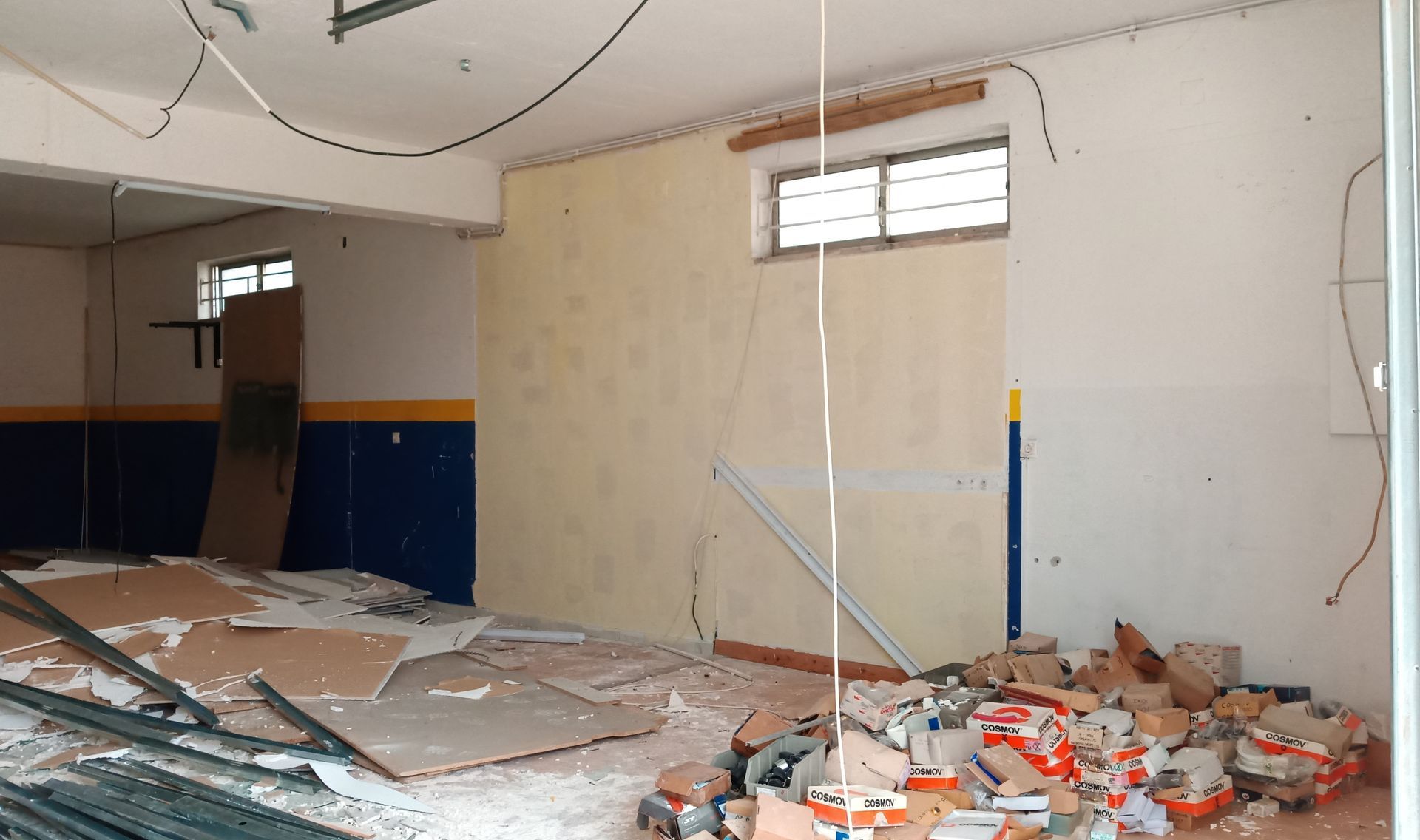 Interior de uma sala em construção, com entulho, paredes expostas e uma janela.