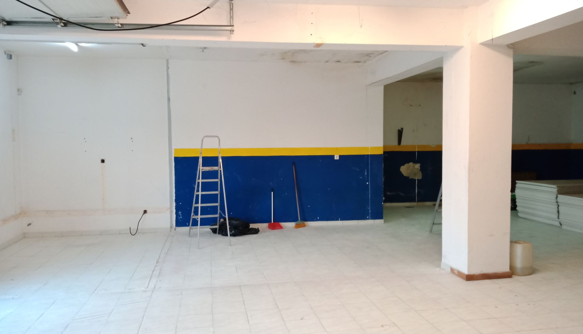 Interior de um quarto vazio com paredes brancas, detalhes em azul e amarelo e uma escada.