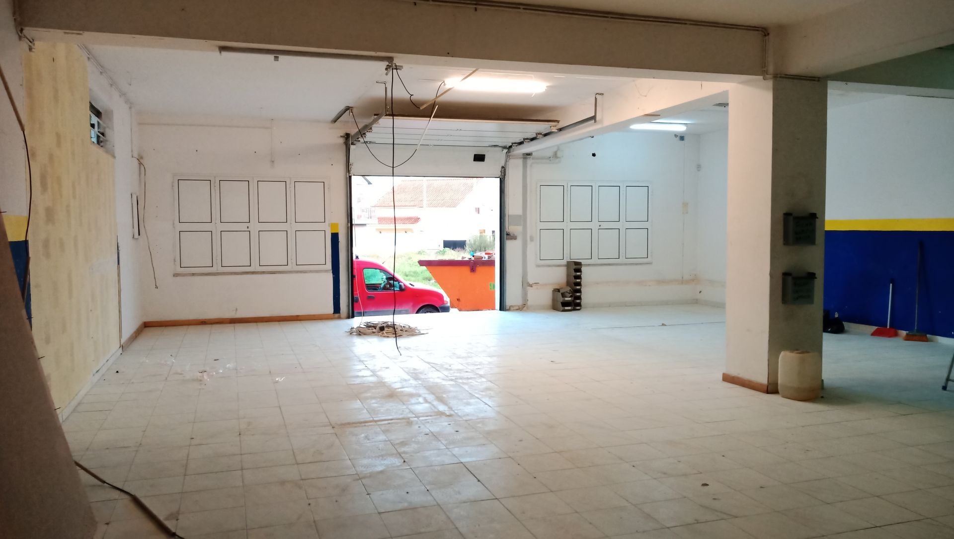 Interior de garagem vazia com porta aberta, carro vermelho visível do lado de fora.