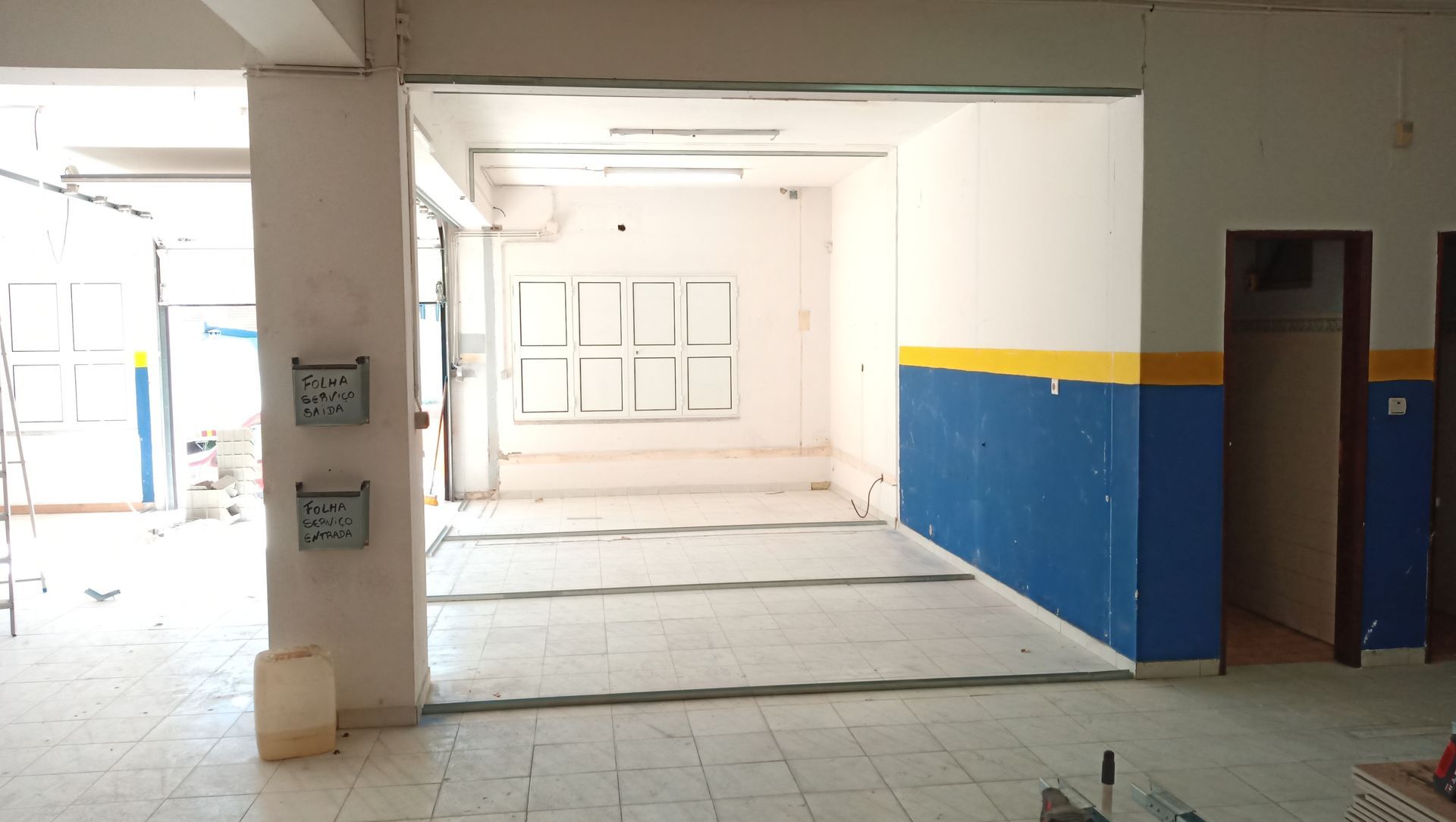 Interior de um quarto com paredes brancas, azuis e amarelas. Piso cinza e portas abertas são visíveis.