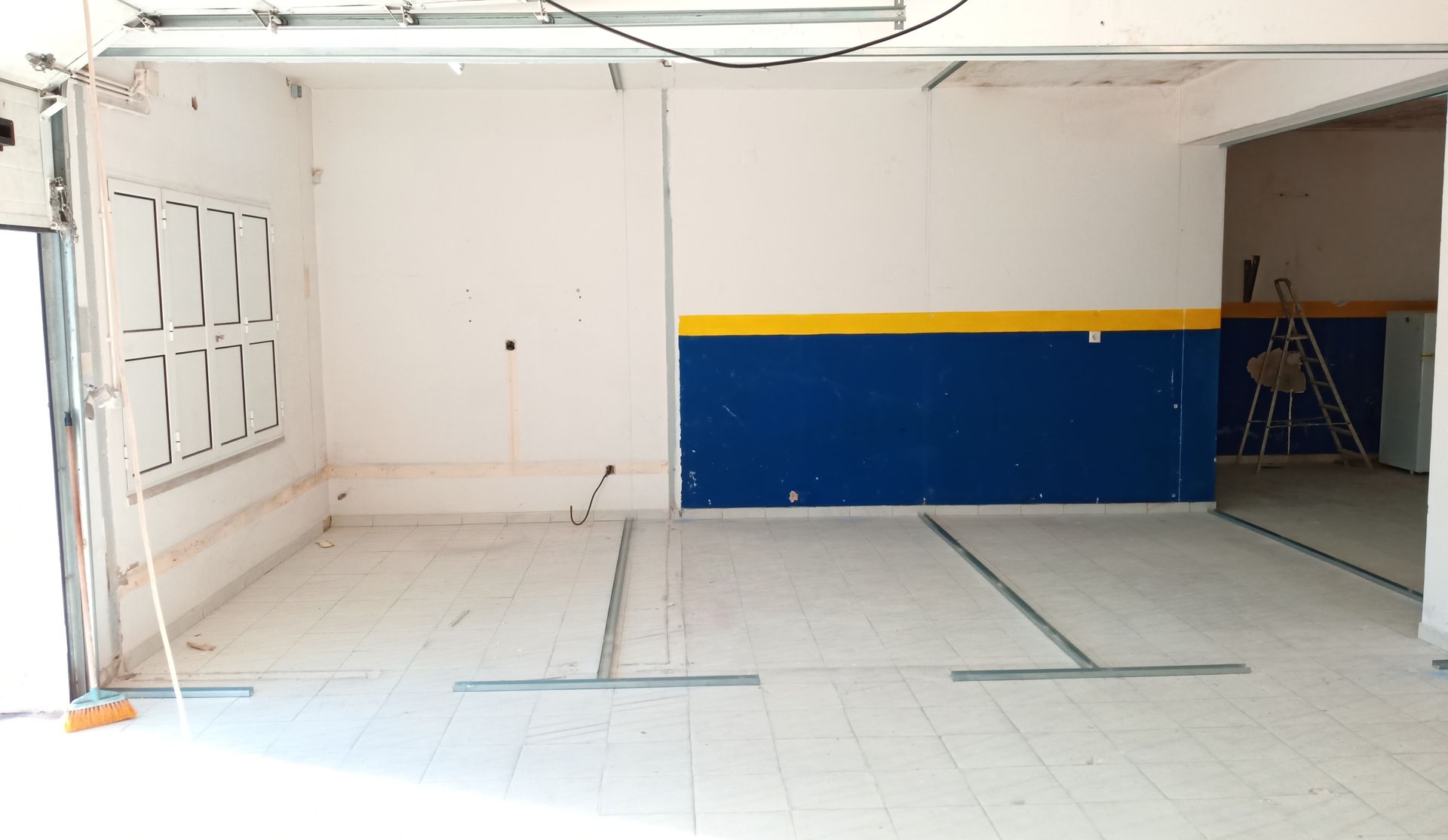 Interior de garagem vazia com paredes brancas e uma parede de destaque em azul e amarelo.
