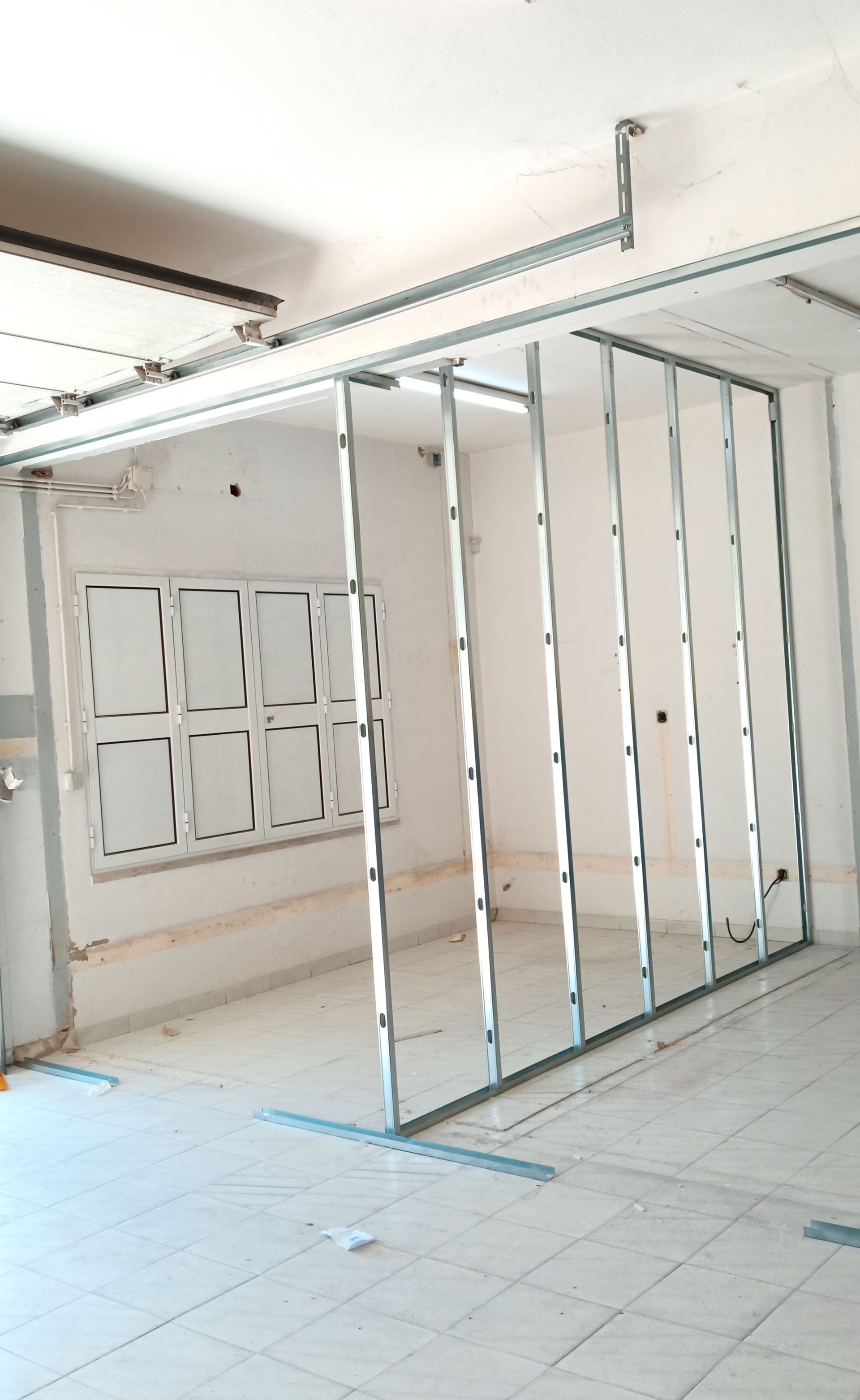 Estrutura metálica para parede divisória, instalada em espaço interior próximo a uma janela.