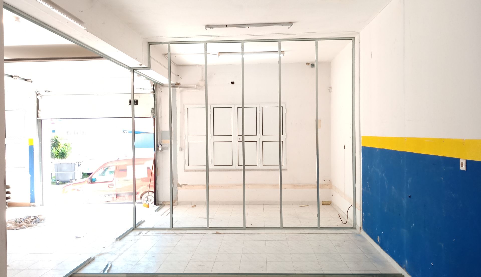 Estrutura metálica para construção de parede interna. Paredes brancas com pintura azul e amarela em um cômodo com janela.