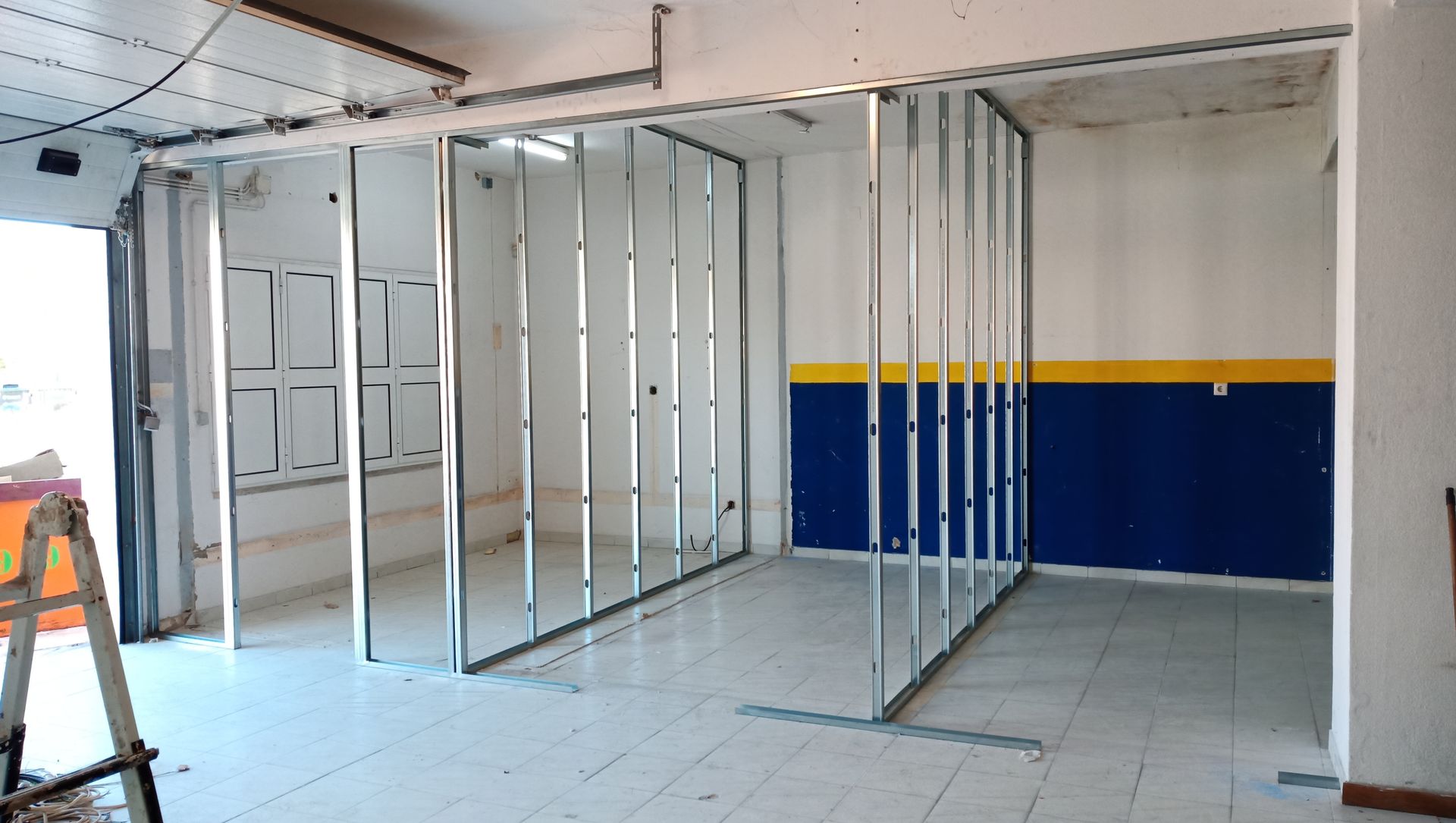 Estrutura metálica para divisória de parede em um cômodo com paredes pintadas de azul e amarelo.