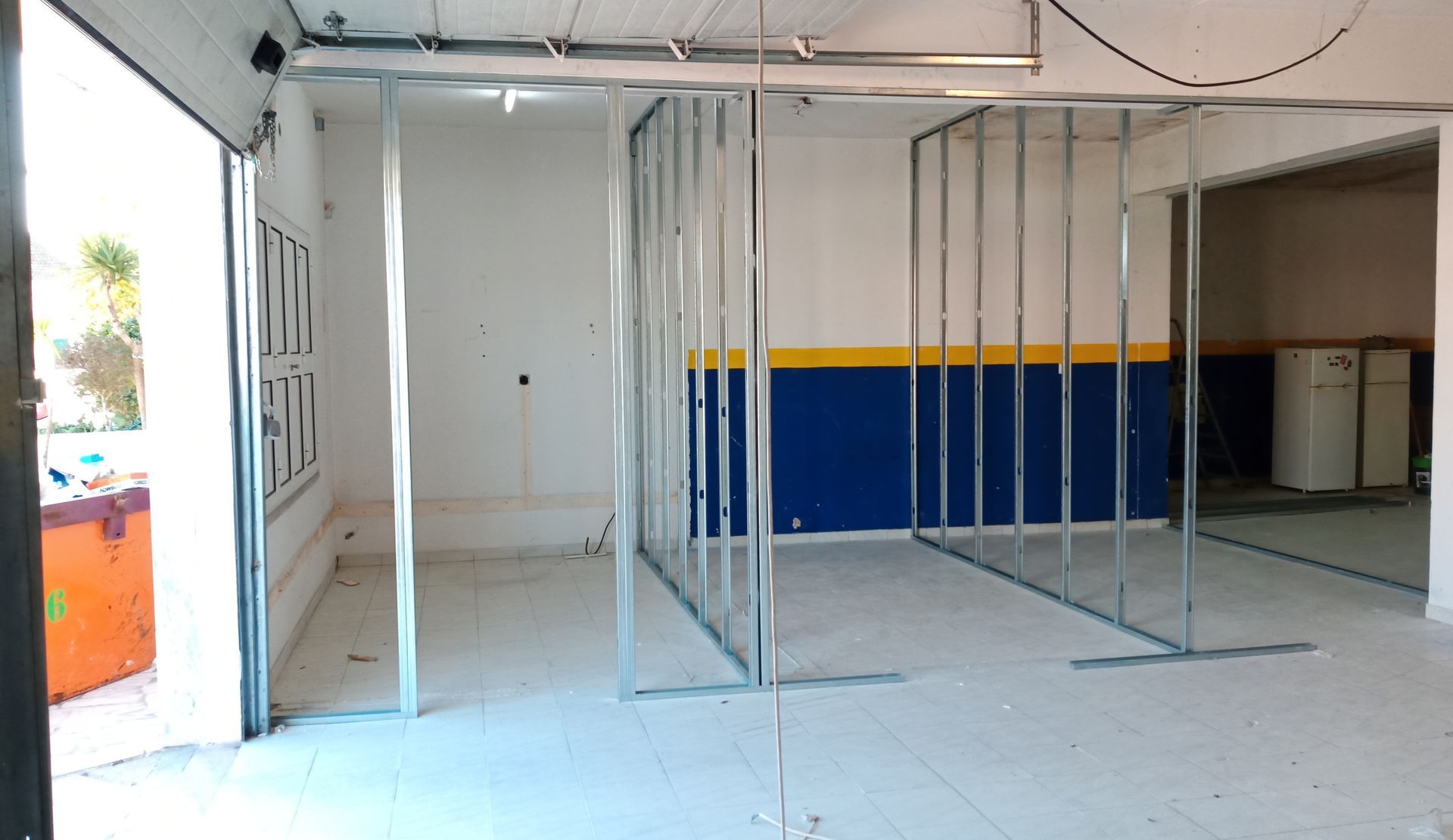 Estrutura metálica para paredes internas em um cômodo com pintura azul e amarela na parede do fundo.