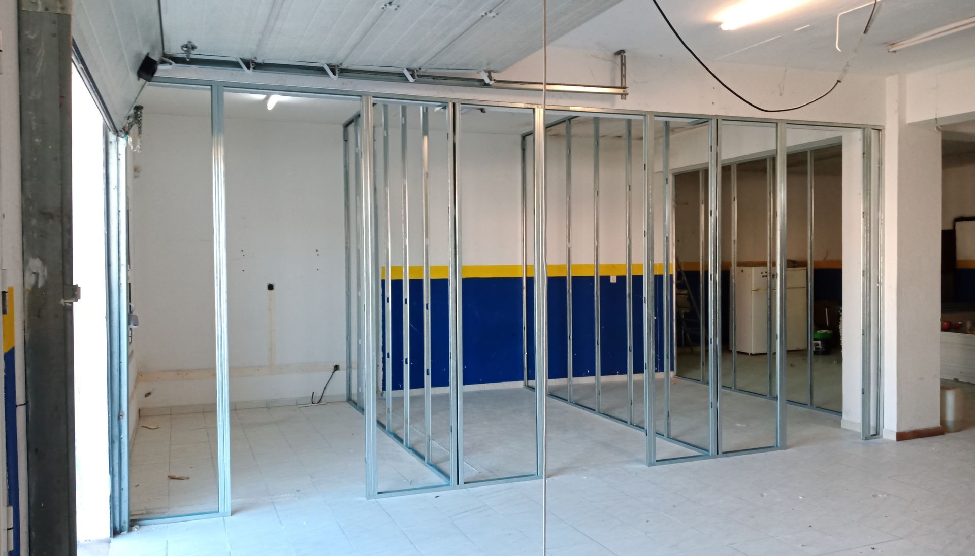 Estrutura metálica para paredes internas de uma garagem com seções pintadas de azul/amarelo.