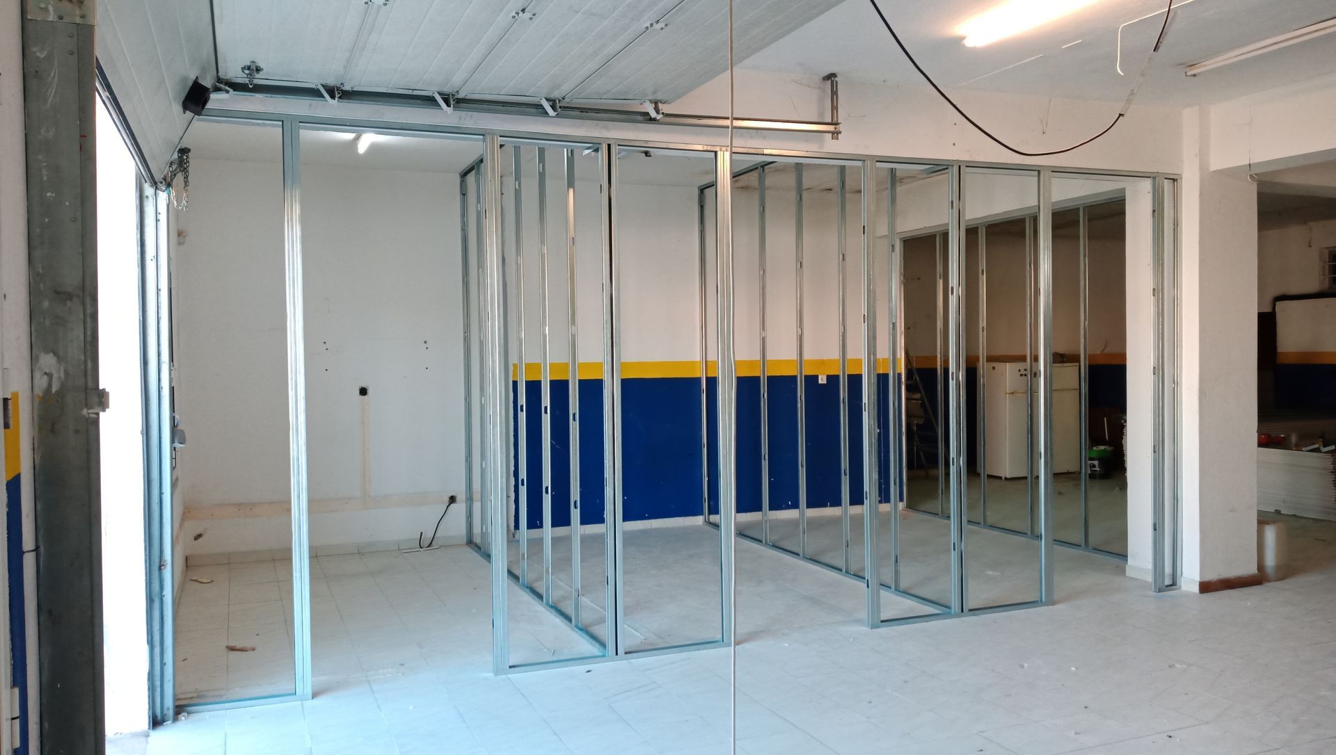 Estrutura metálica para paredes internas em um espaço tipo garagem com detalhes em azul e amarelo.