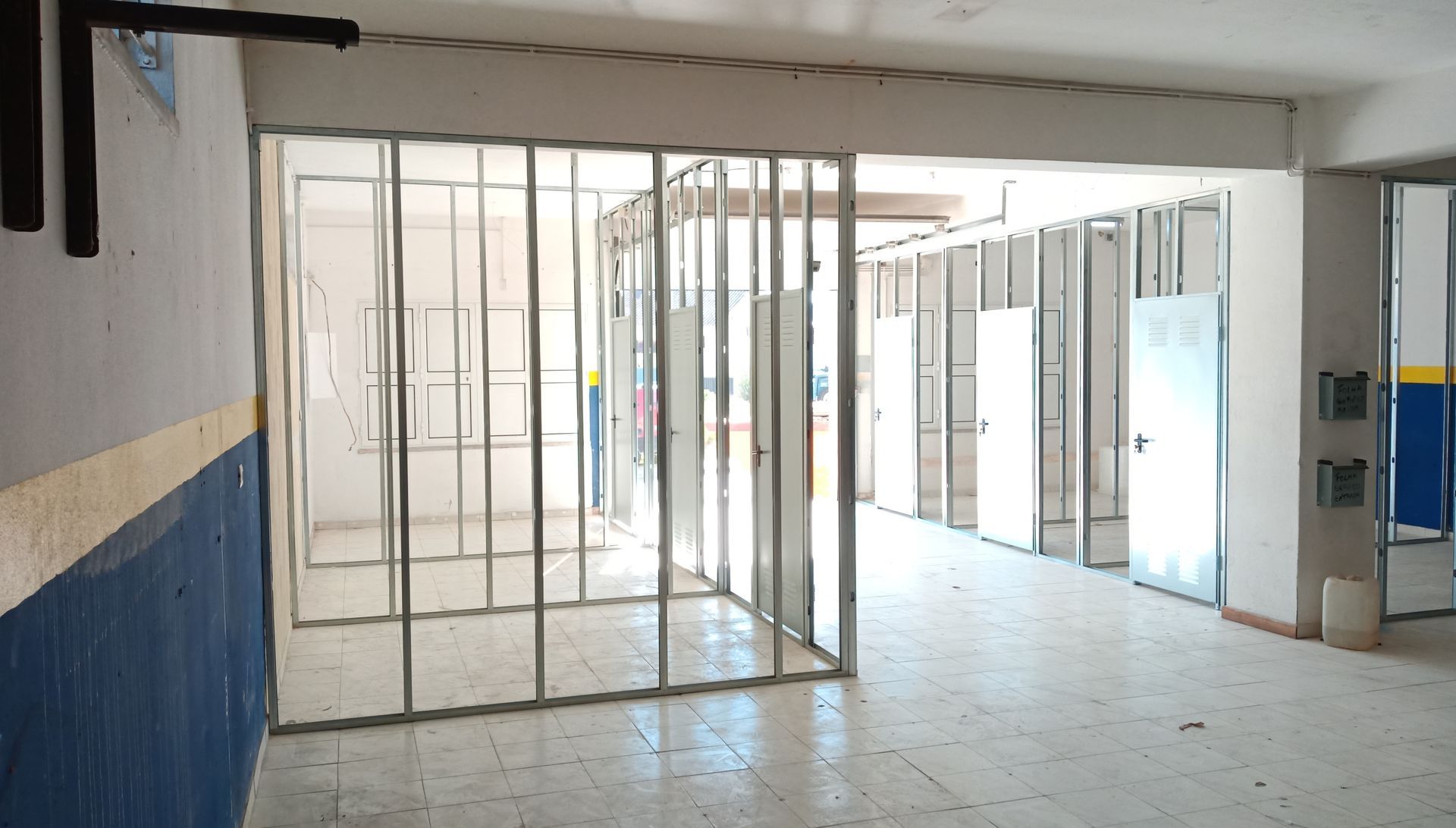 Estrutura metálica para paredes e portas no corredor de um edifício. Espaço amplo e iluminado.