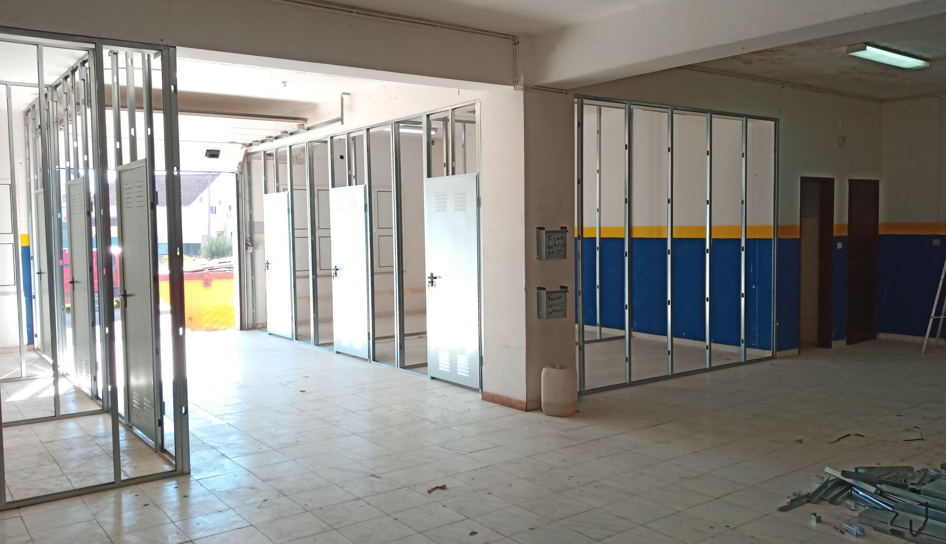 Construção interior; estrutura metálica para novas paredes e diversas portas. Paredes existentes pintadas de azul e amarelo.