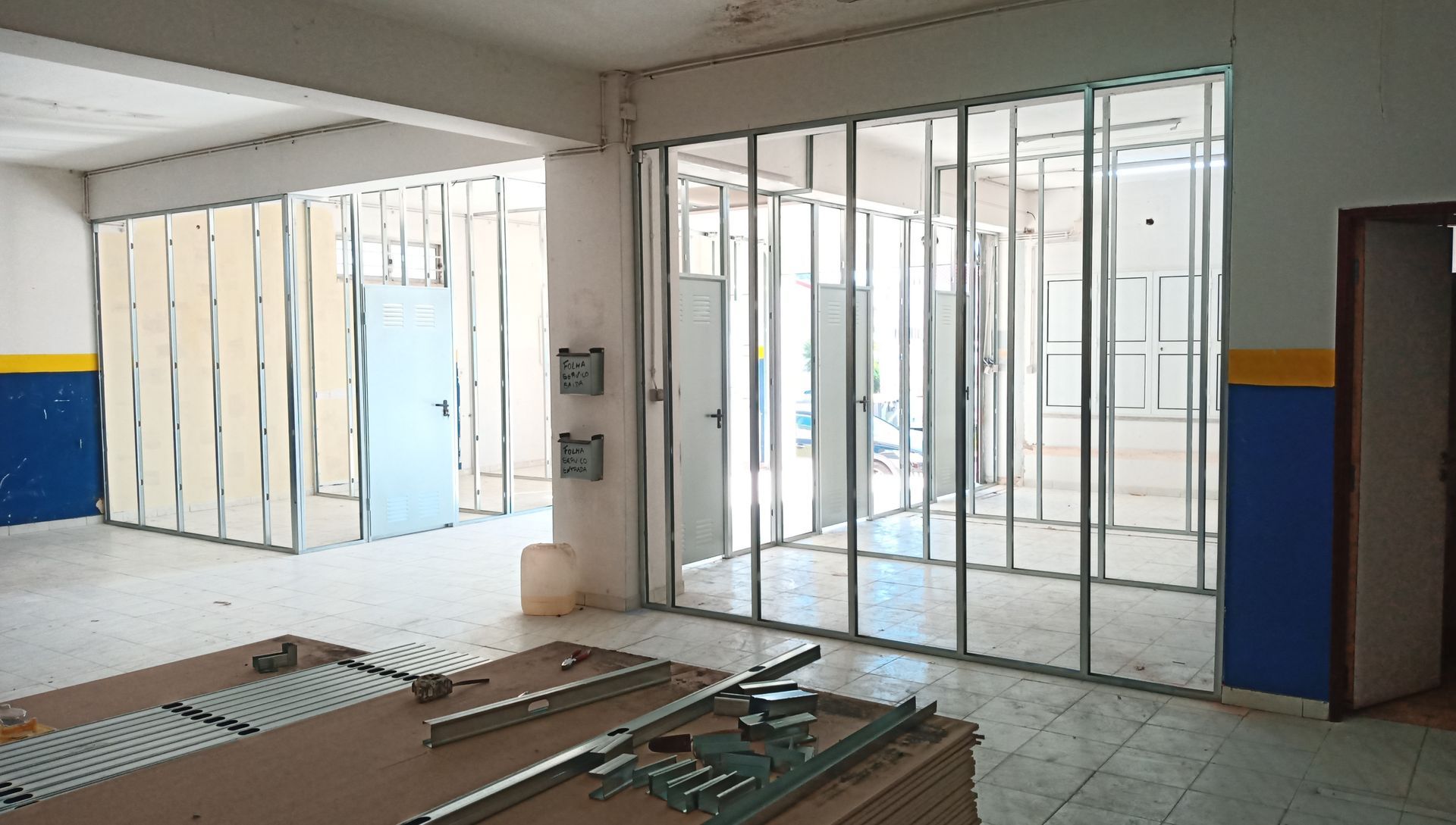 Quarto interior em construção, com estrutura metálica para as paredes, em estado inacabado visível. Paredes pintadas de azul e amarelo.