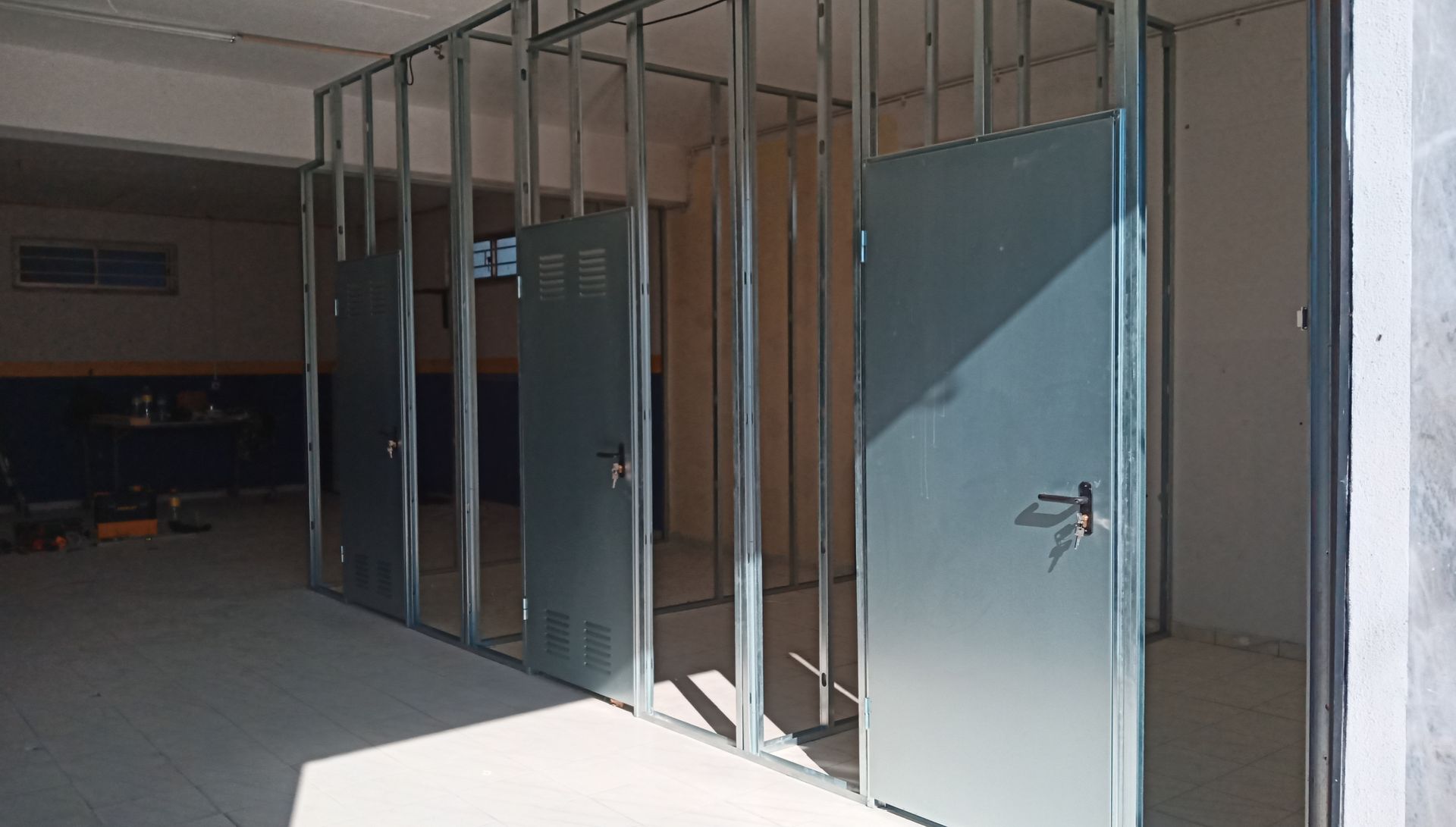 Paredes com estrutura metálica e portas no interior de um canteiro de obras.