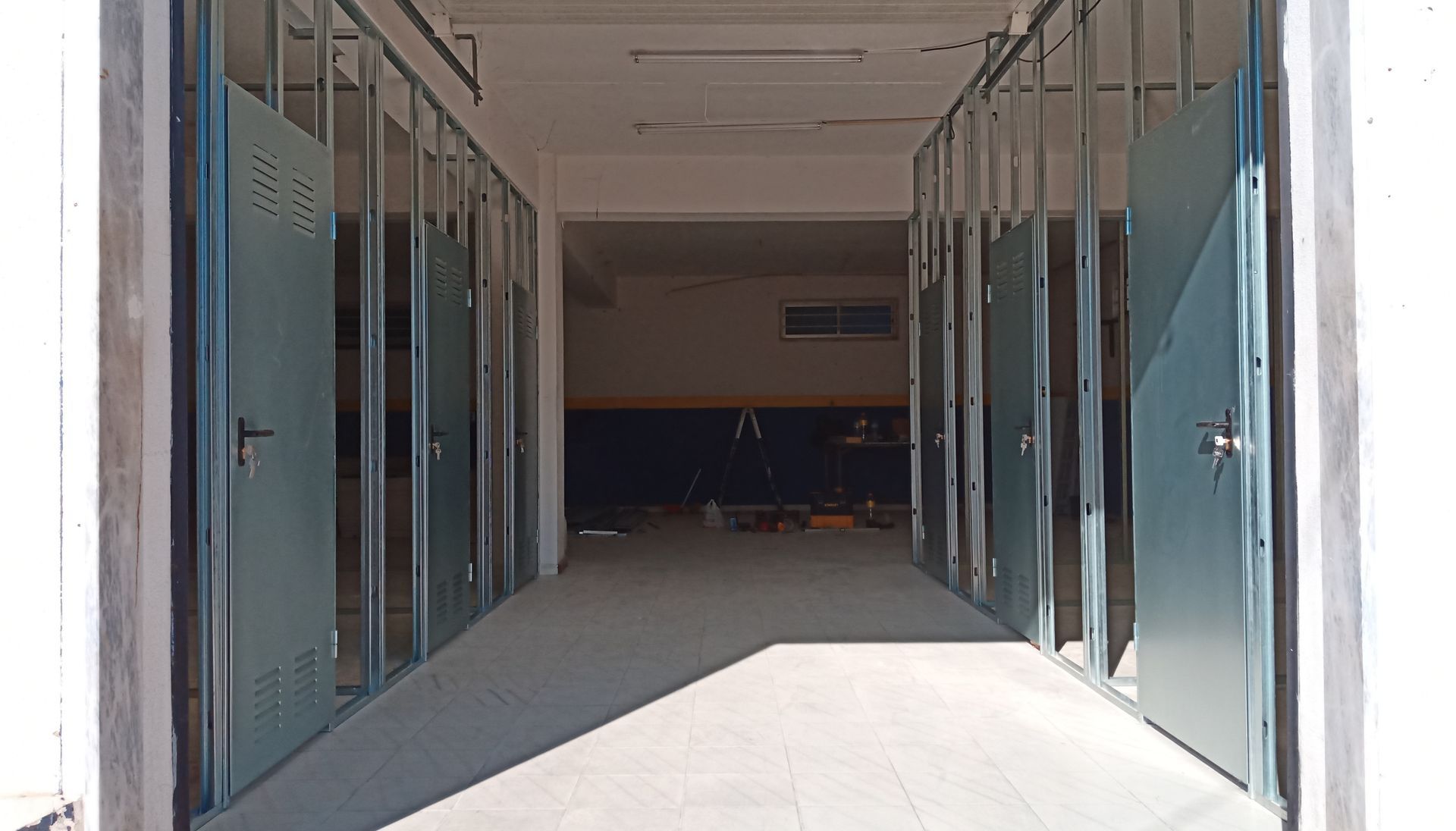 Portas de metal abertas dão acesso a um corredor pouco iluminado. A luz entra pela porta.