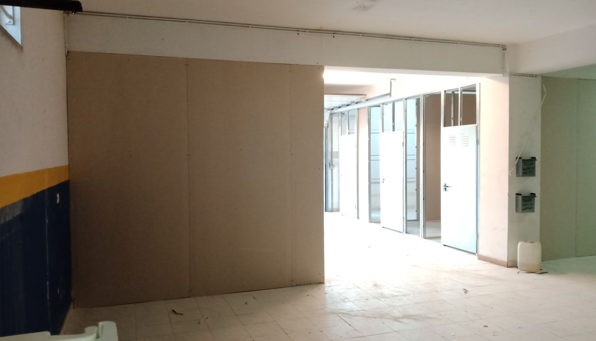 Vista interior de um edifício com uma grande abertura, paredes inacabadas e um corredor.