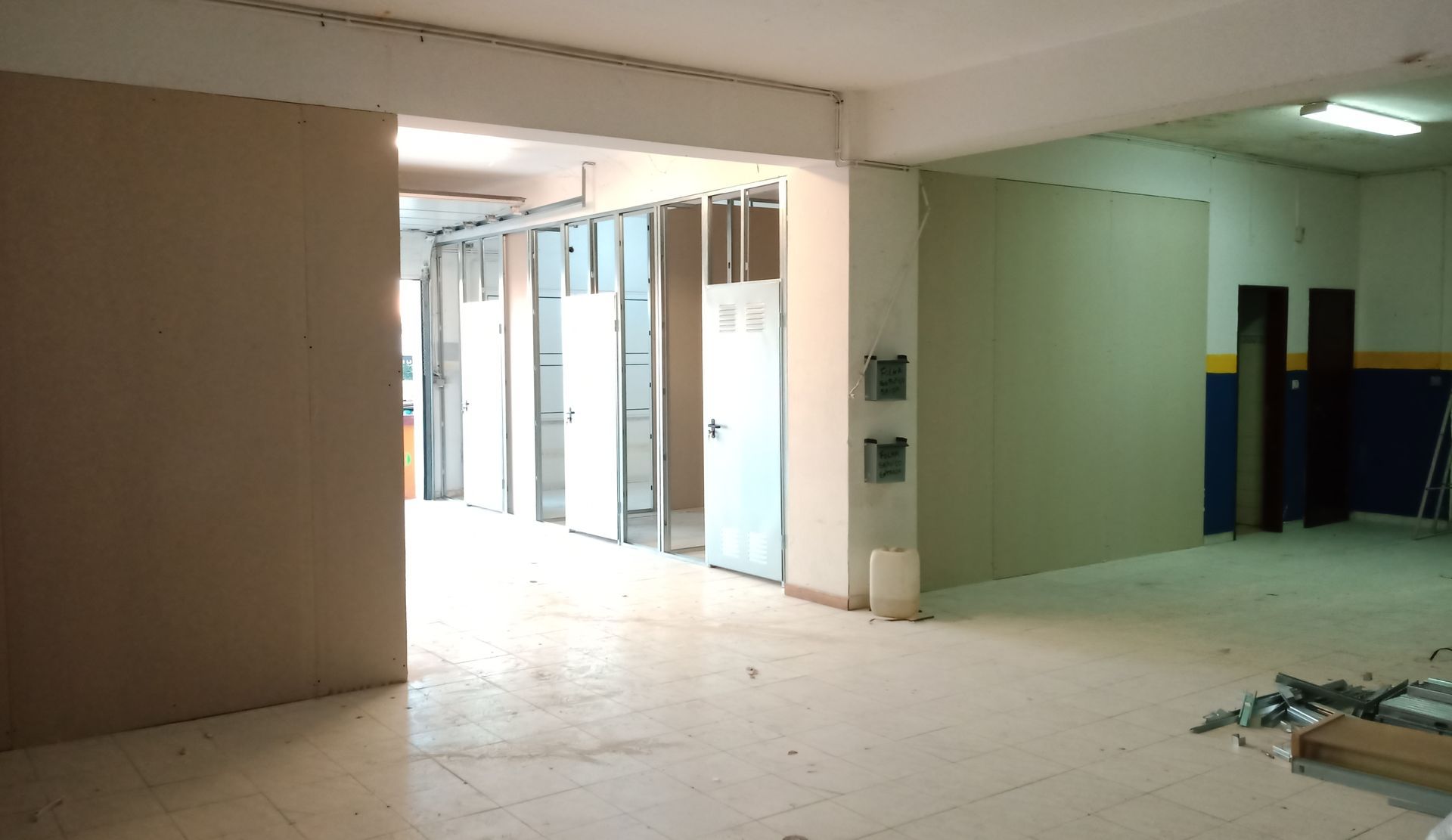 Vista interna de um cômodo em construção, com portas, paredes inacabadas e entulho espalhado pelo chão.