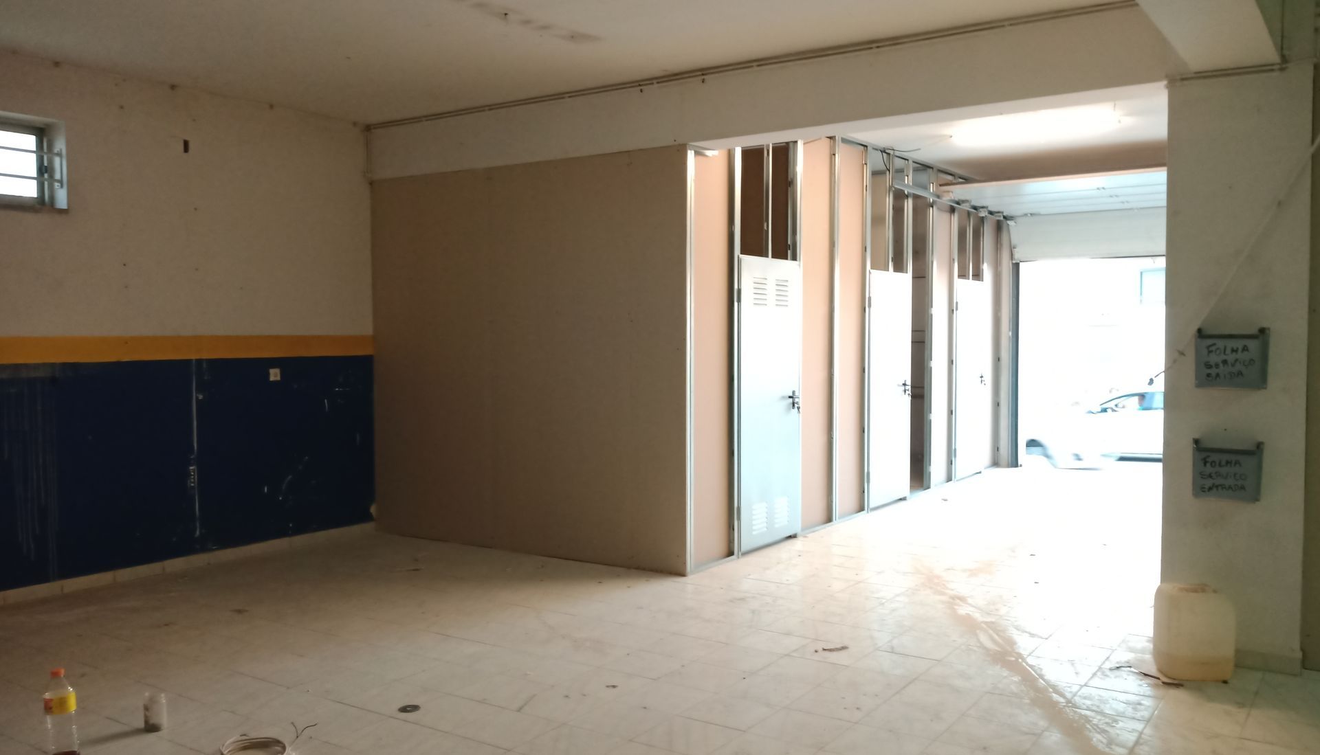 Interior de um cômodo em construção com paredes parcialmente erguidas, uma porta aberta e uma janela.