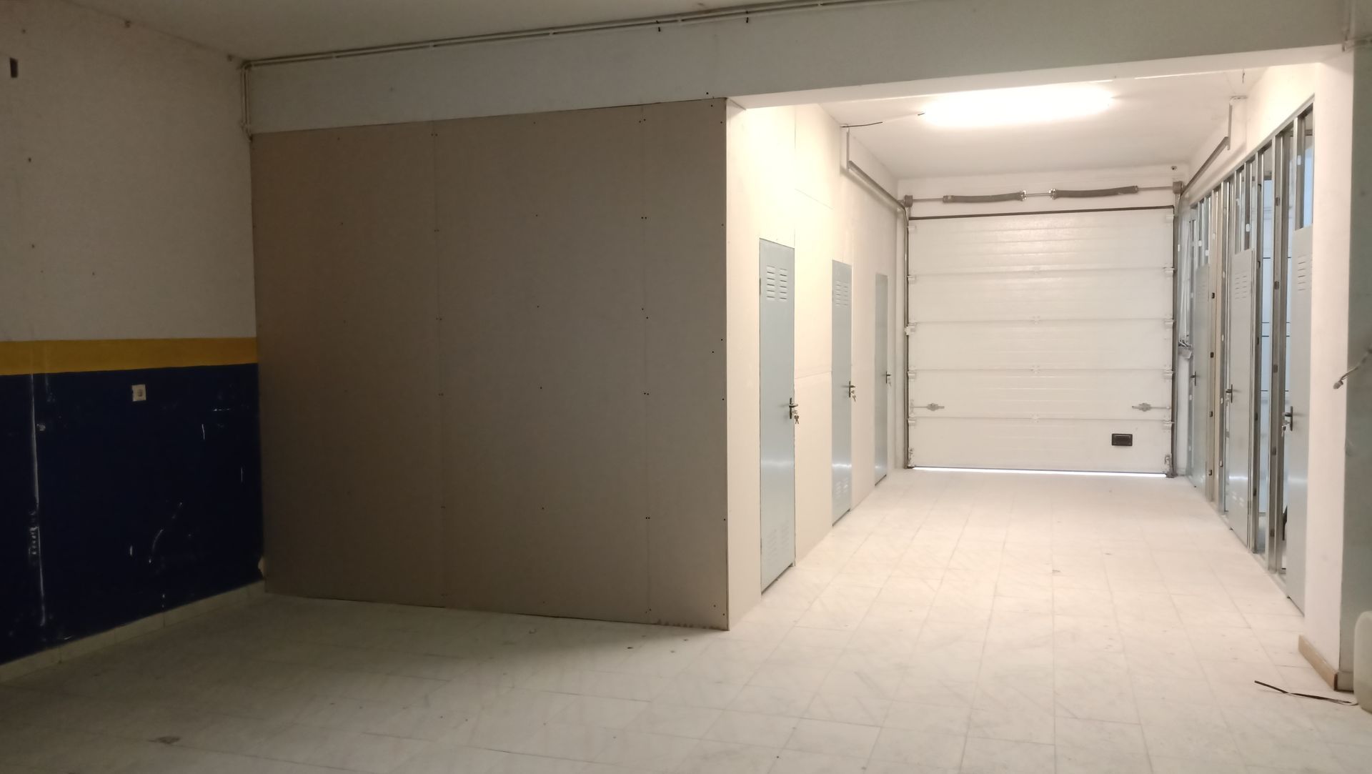 Espaço comercial vazio com paredes de gesso, porta de garagem e entradas.