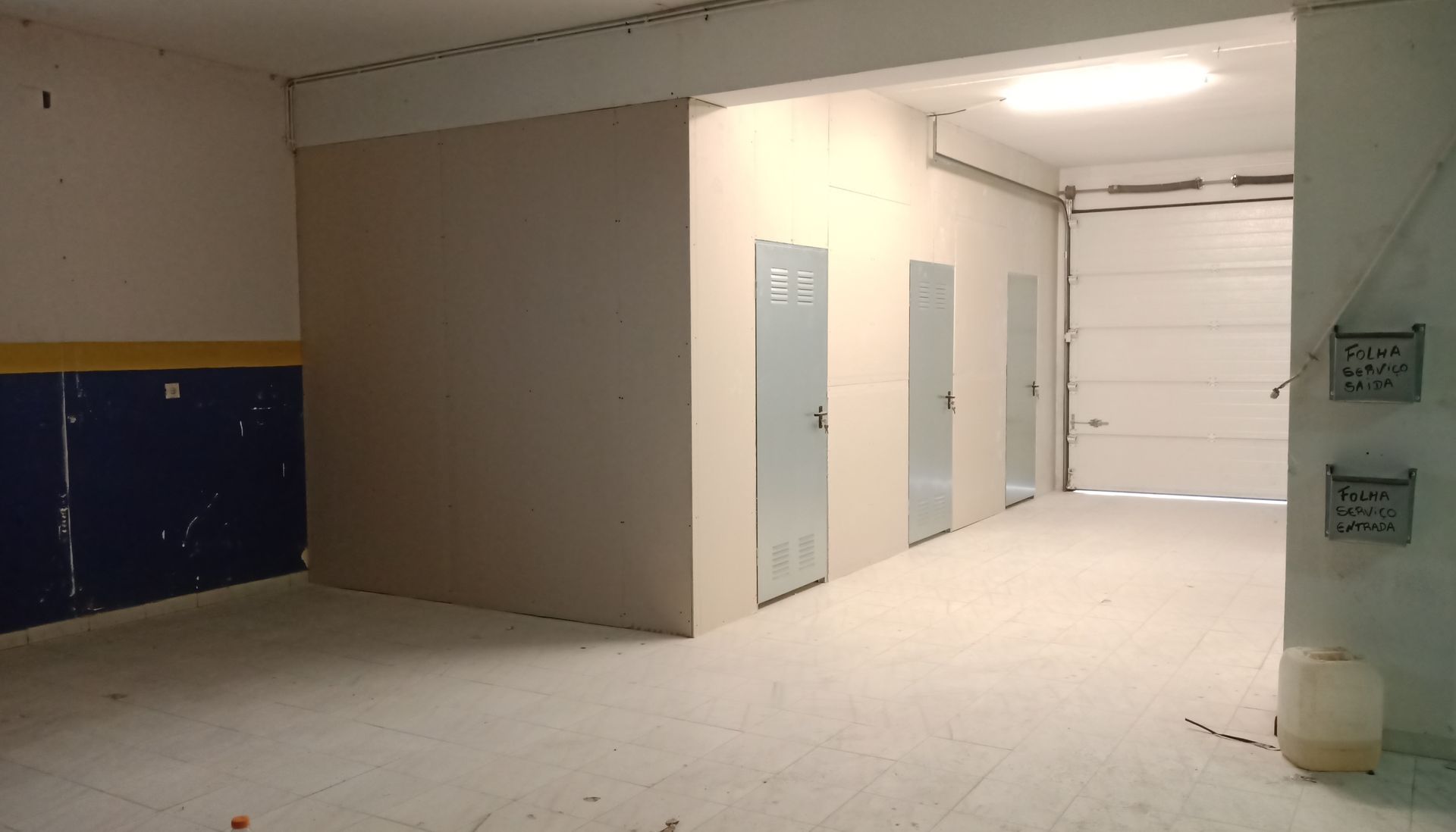 Interior de um depósito com várias portas, incluindo uma porta de garagem, paredes pintadas e piso de concreto.