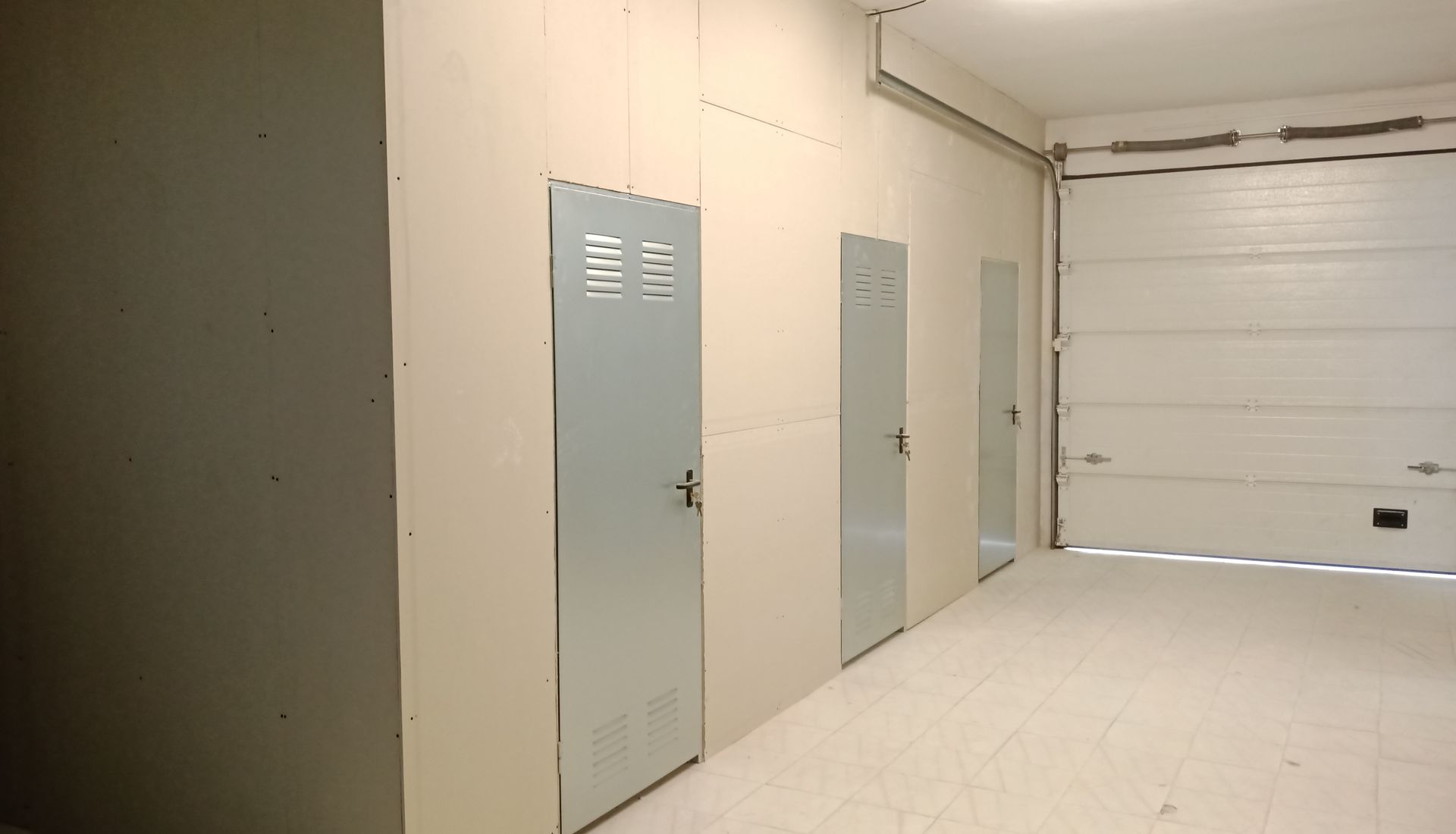 Interior de um depósito com portas de metal e uma grande porta de garagem. As paredes são de cor branco-sujo.