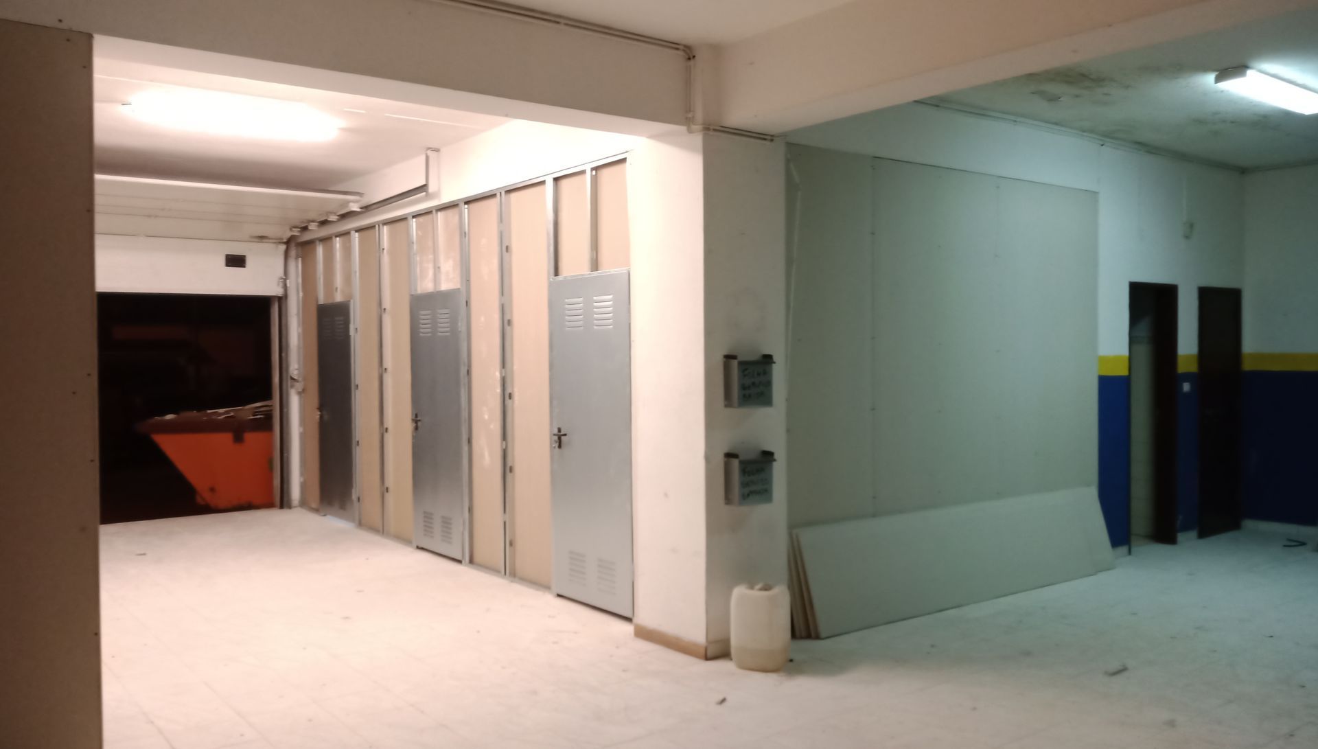 Espaço interno em construção com paredes de gesso acartonado e portas de metal.