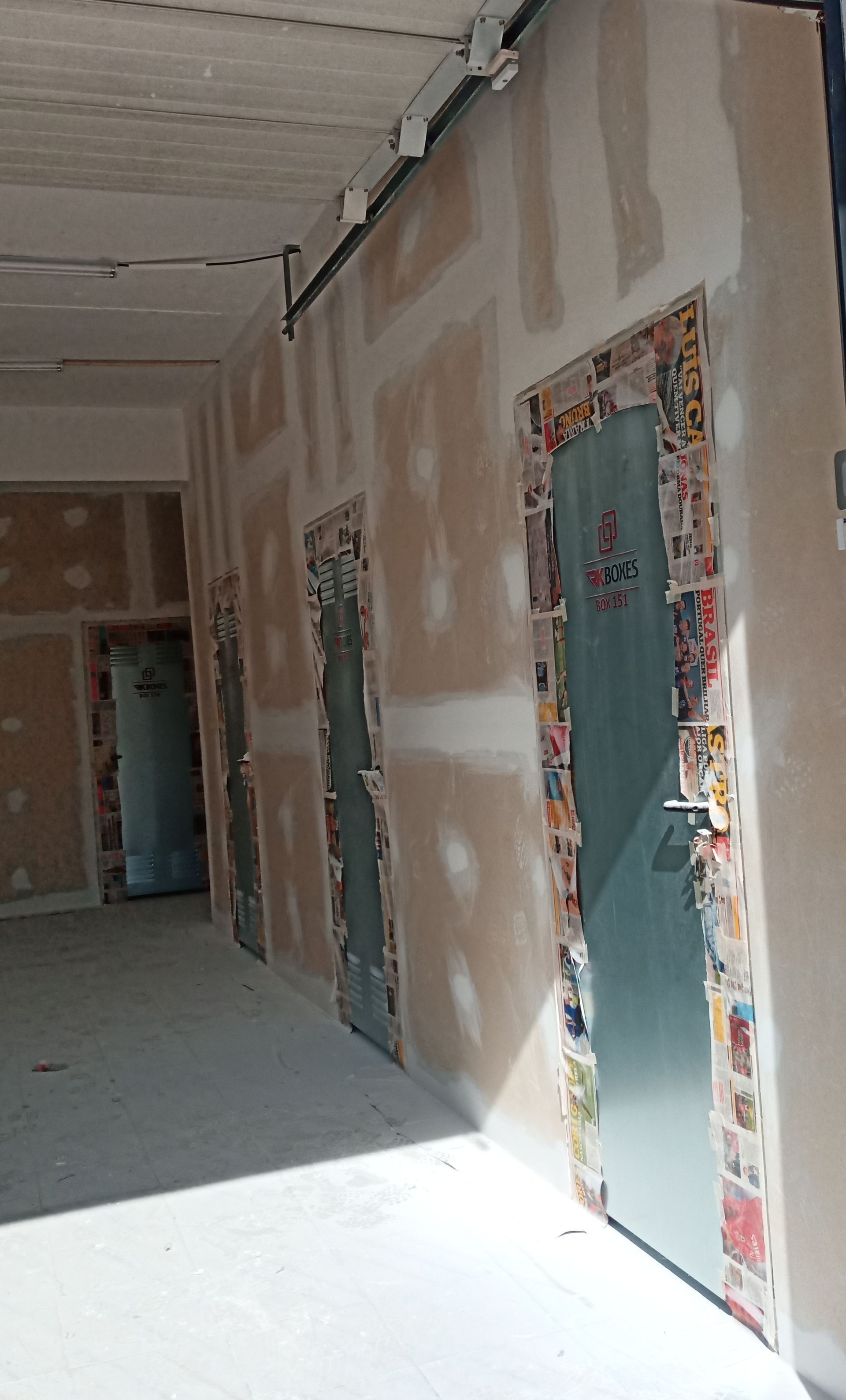 Corredor com três portas verde-azuladas, com detalhes em jornal nas molduras. As paredes são de gesso acartonado.