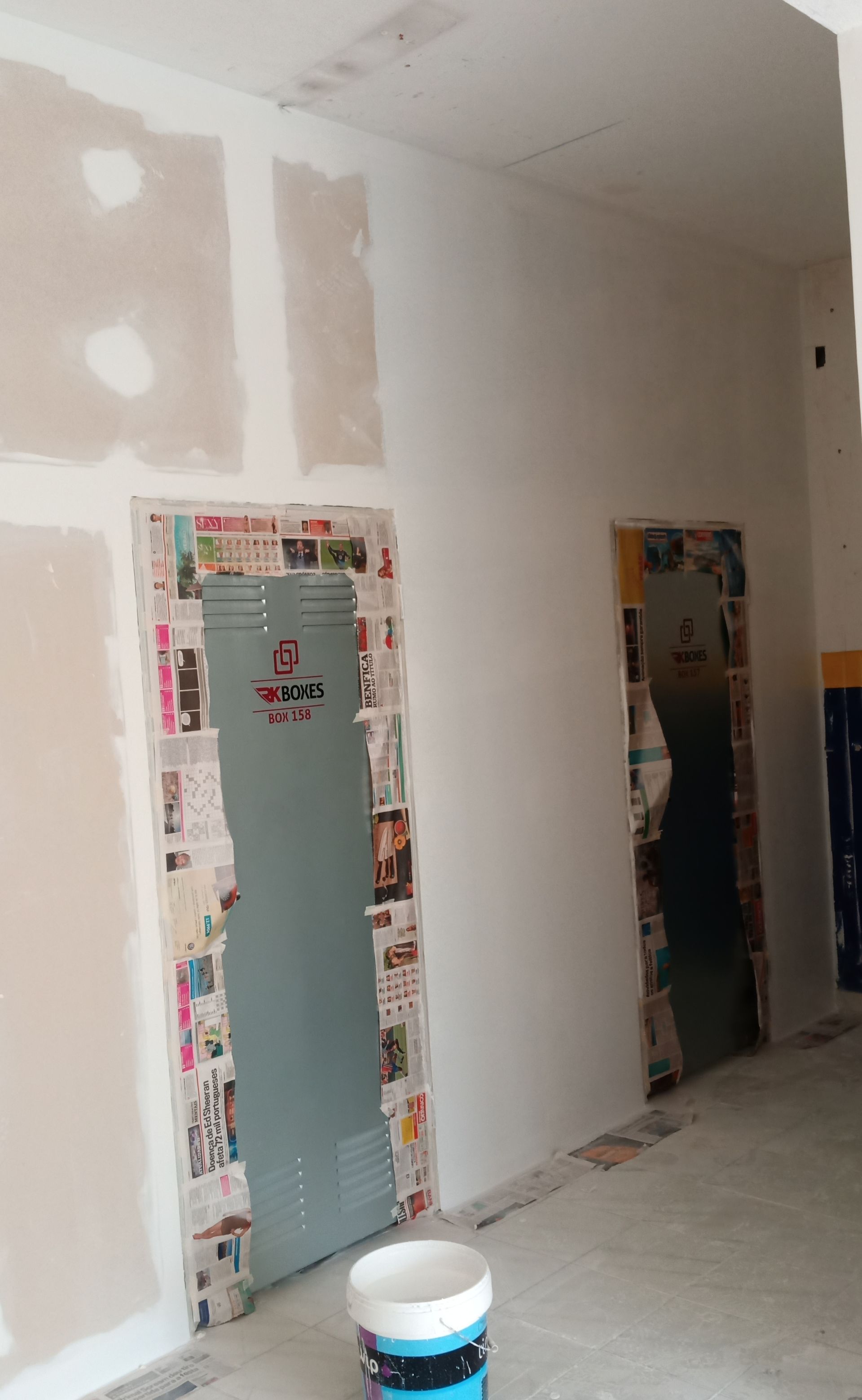 Construção de parede interna com drywall, portas vedadas com jornal e um balde de tinta.