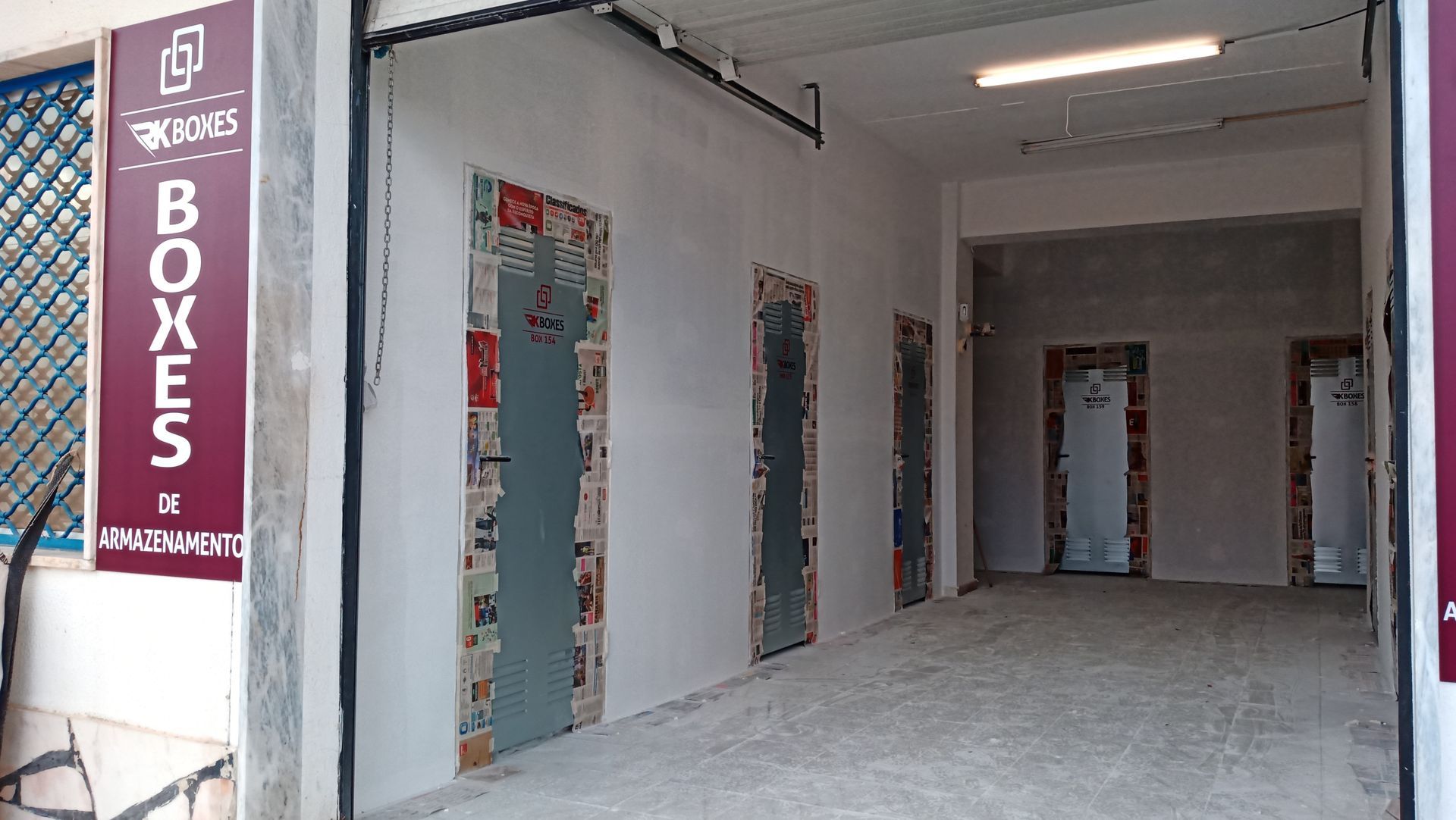 Entrada para unidades de armazenamento, paredes brancas, piso de concreto, placa marrom com a palavra 