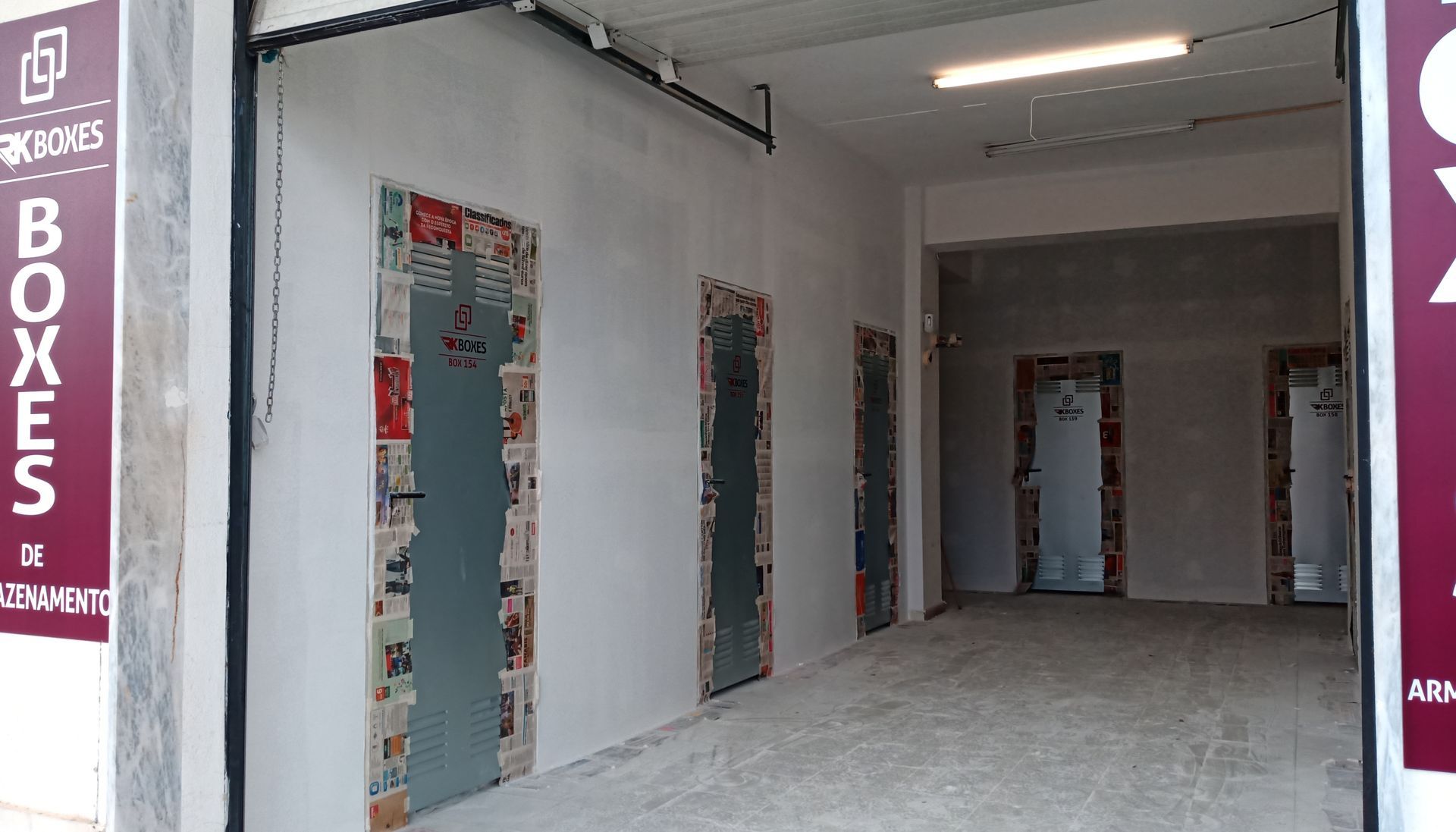 Vista interna de um depósito com várias portas emolduradas por jornais coloridos.