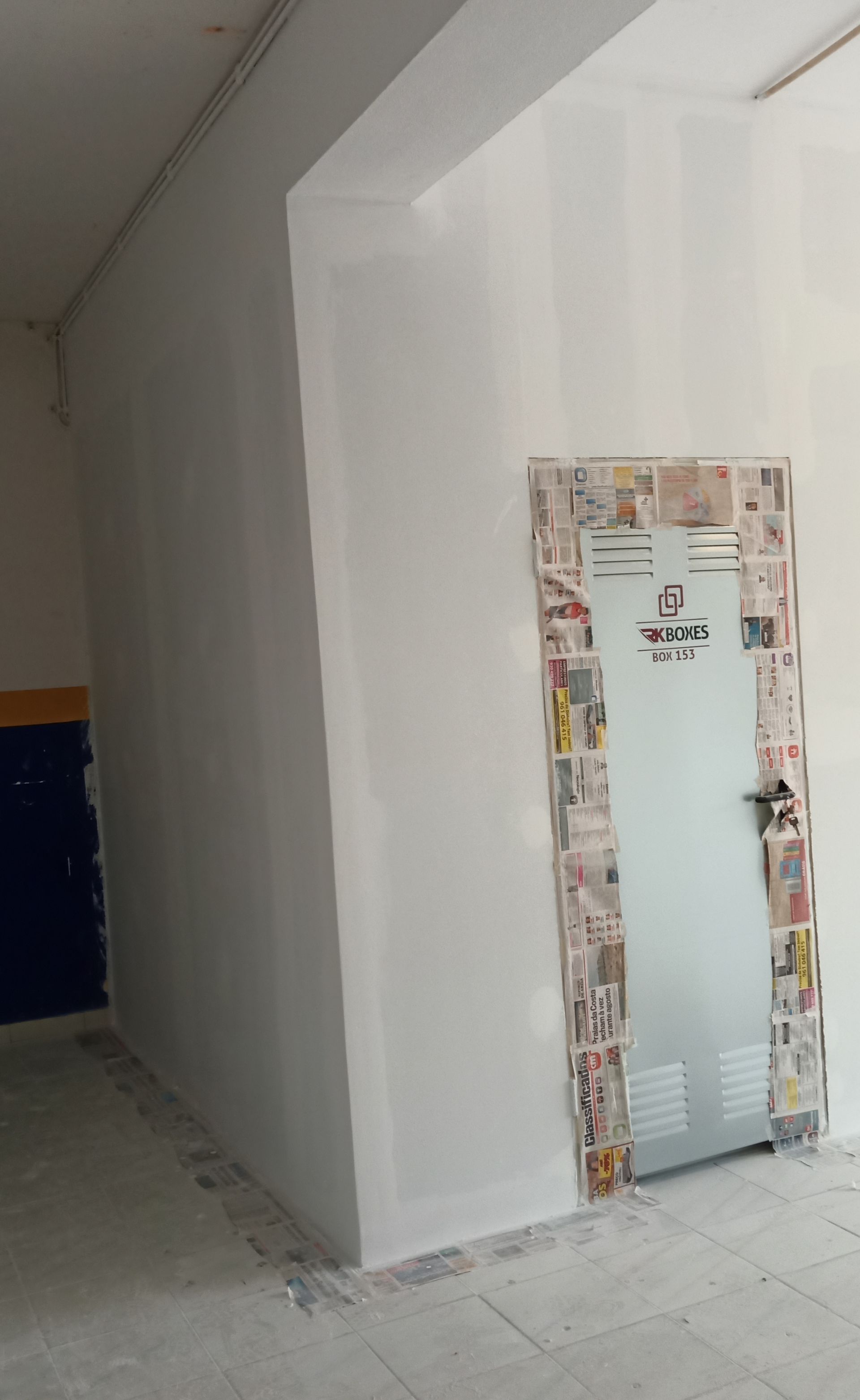 Paredes e porta pintadas de branco em um corredor. Batente da porta decorado com tiras de jornal.