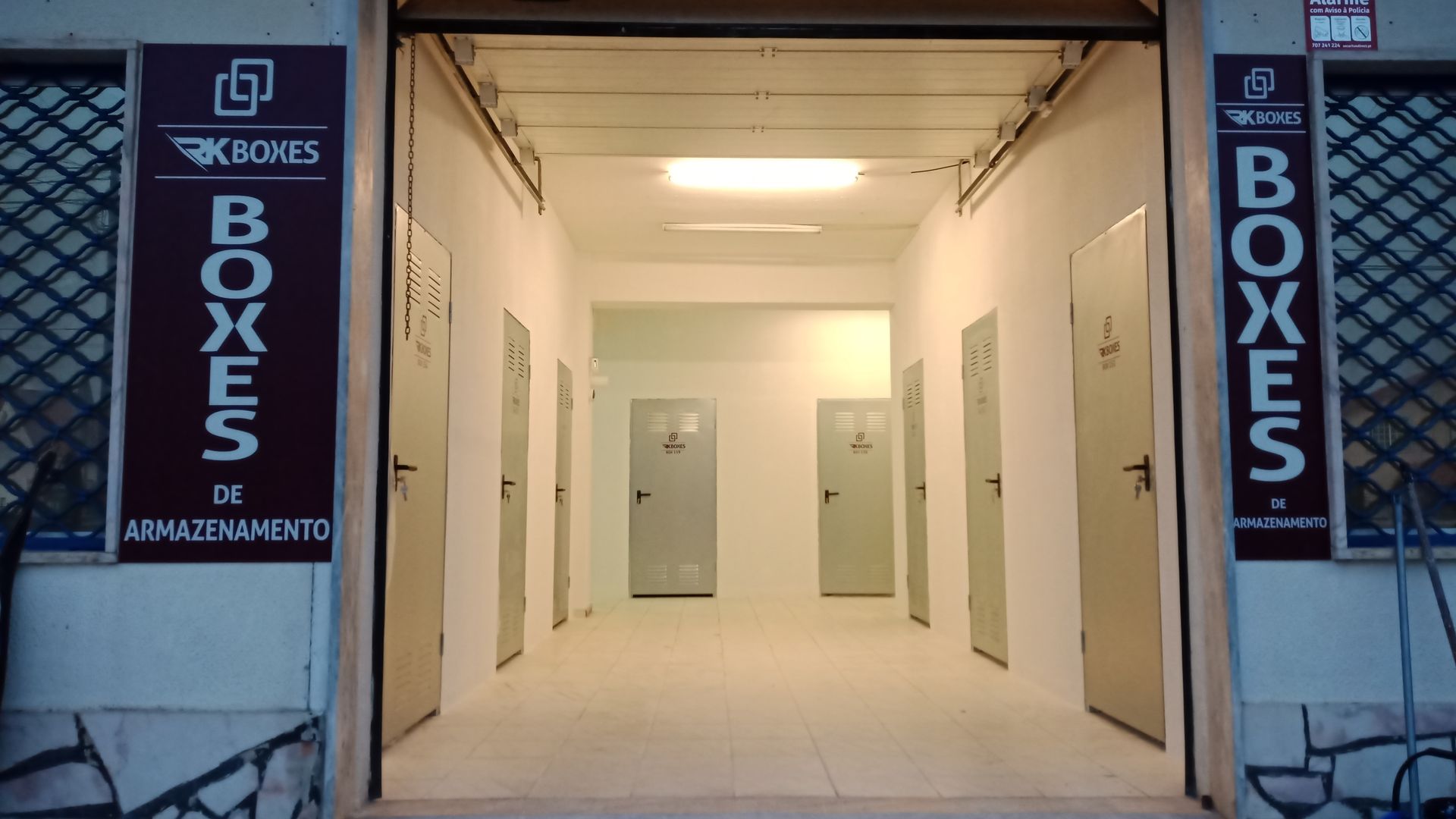 Entrada para os depósitos, portas cinzentas alinham-se num corredor branco, com sinalização em ambos os lados.