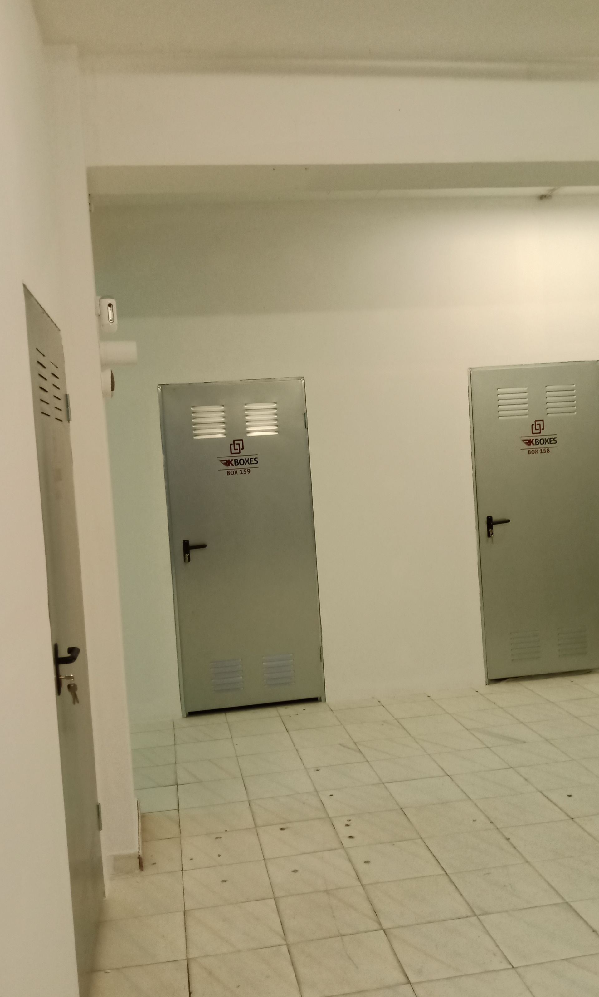 Corredor com três portas prateadas e piso de azulejos. Paredes e teto brancos.