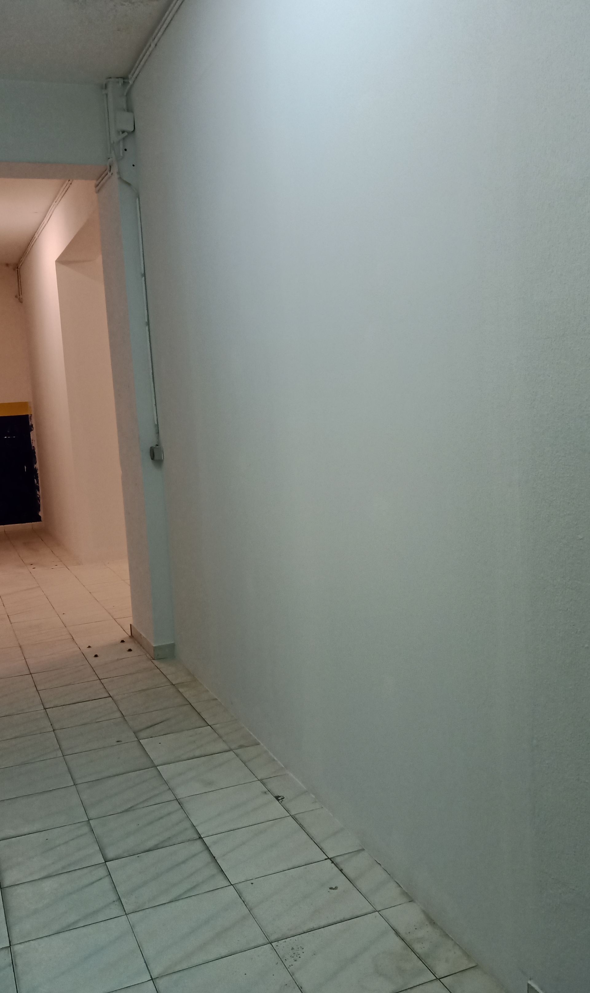 Corredor comprido com paredes brancas e piso de azulejo.