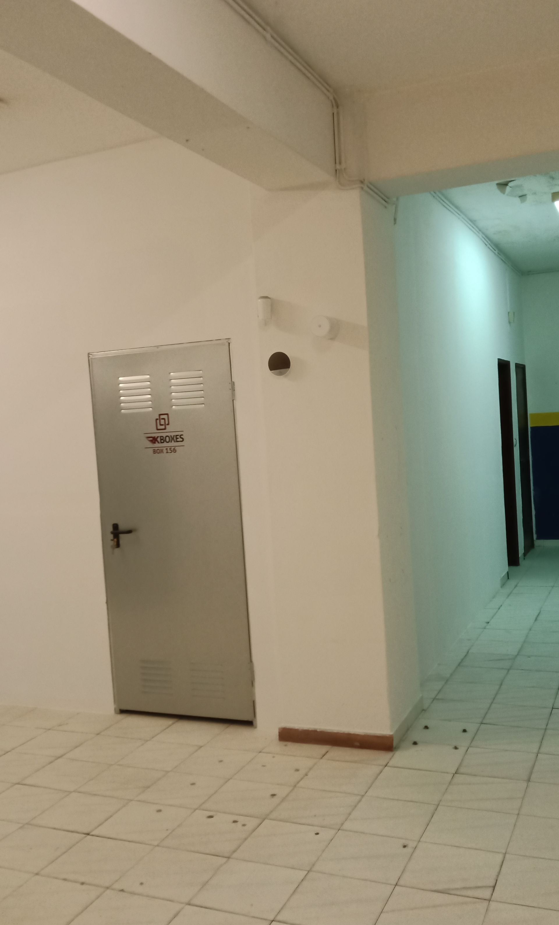 Um corredor com uma porta de metal fechada e um corredor mais longo à direita.