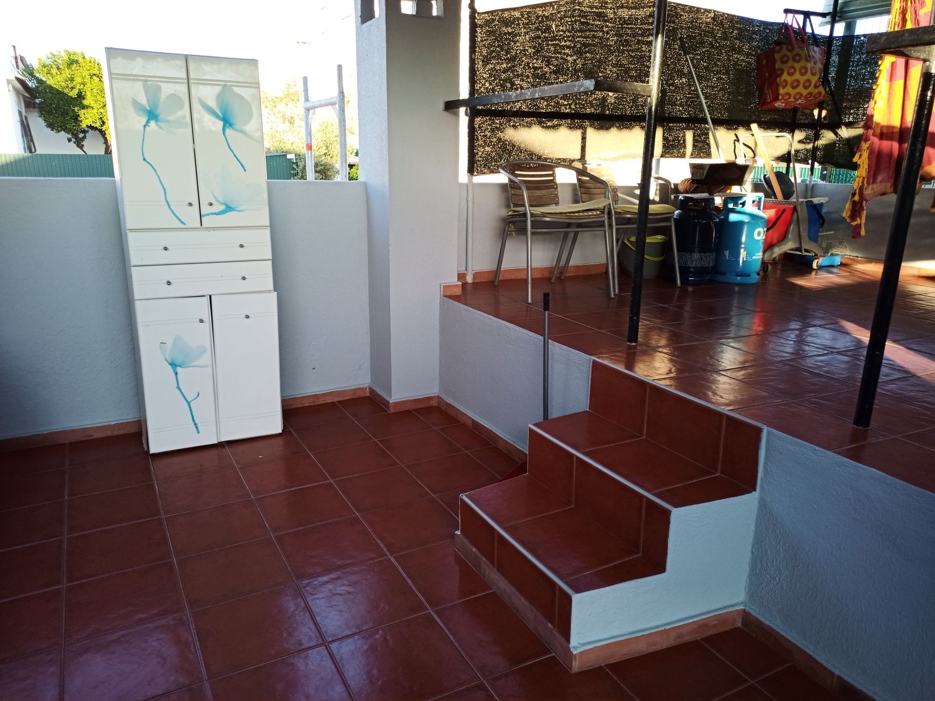 Terraço com piso de azulejo, armário, degraus e itens para área externa.