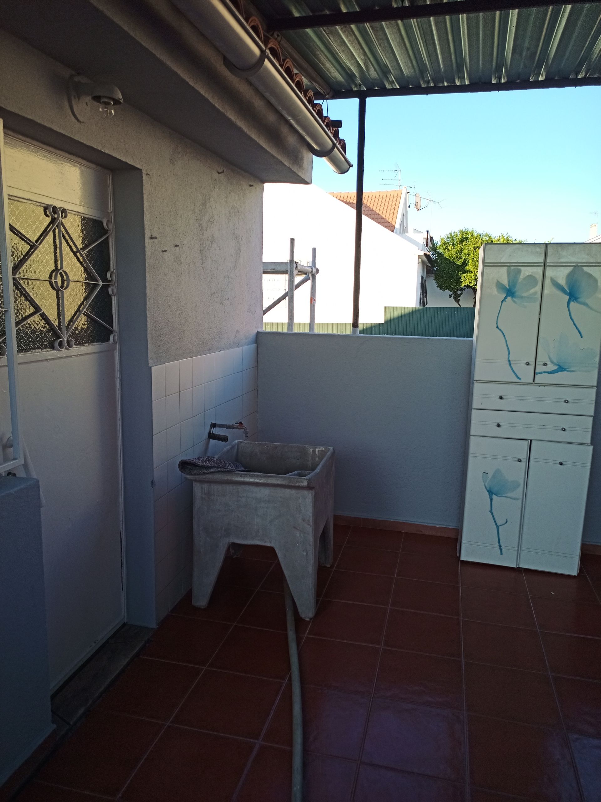 Pátio externo com pia, armário e vista para o prédio e o céu azul.