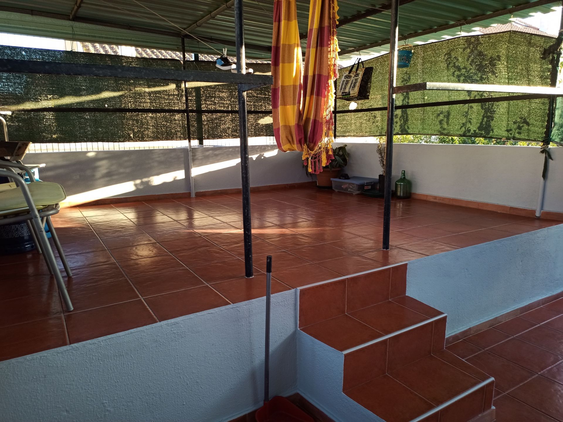 Terraço na cobertura com azulejos, degraus, postes de metal e rede.