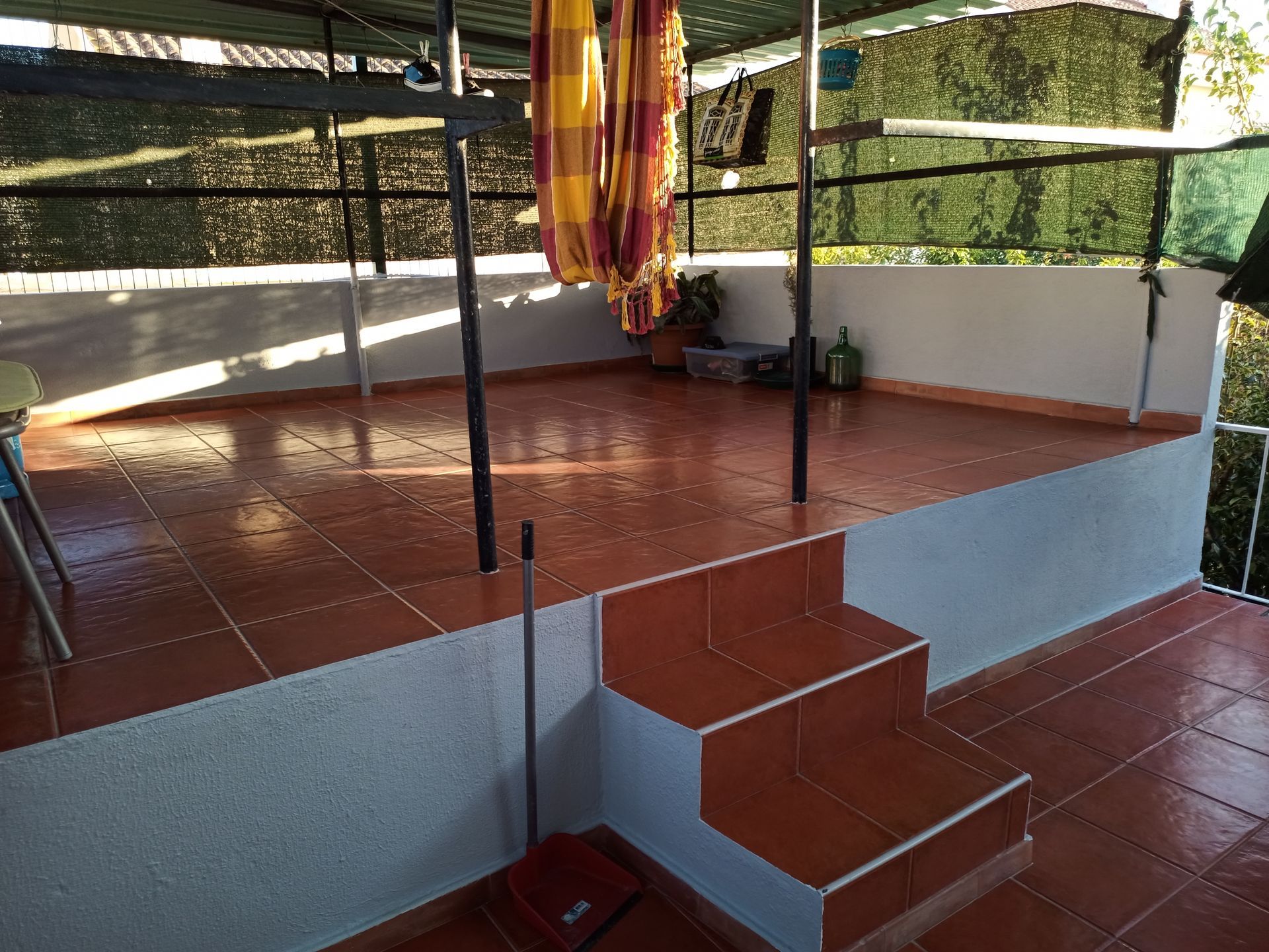 Terraço com telhas de terracota, degraus, rede e estrutura de sombreamento.
