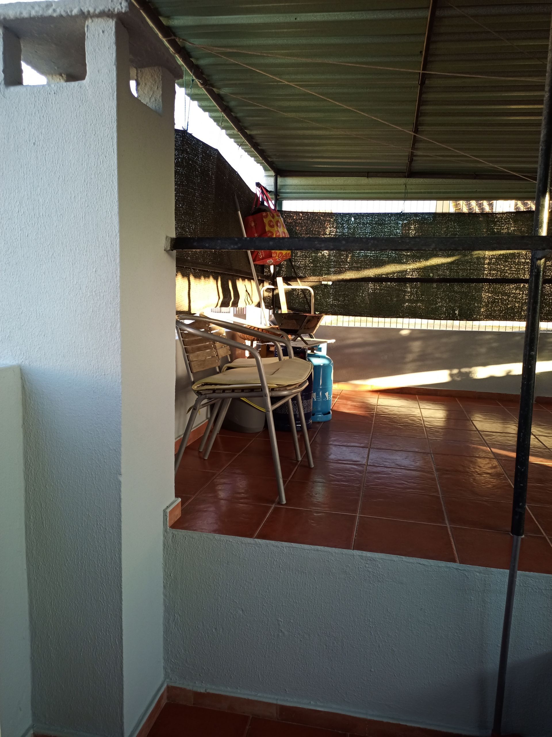 Pátio externo coberto com mesa, cadeiras e botijão de gás.