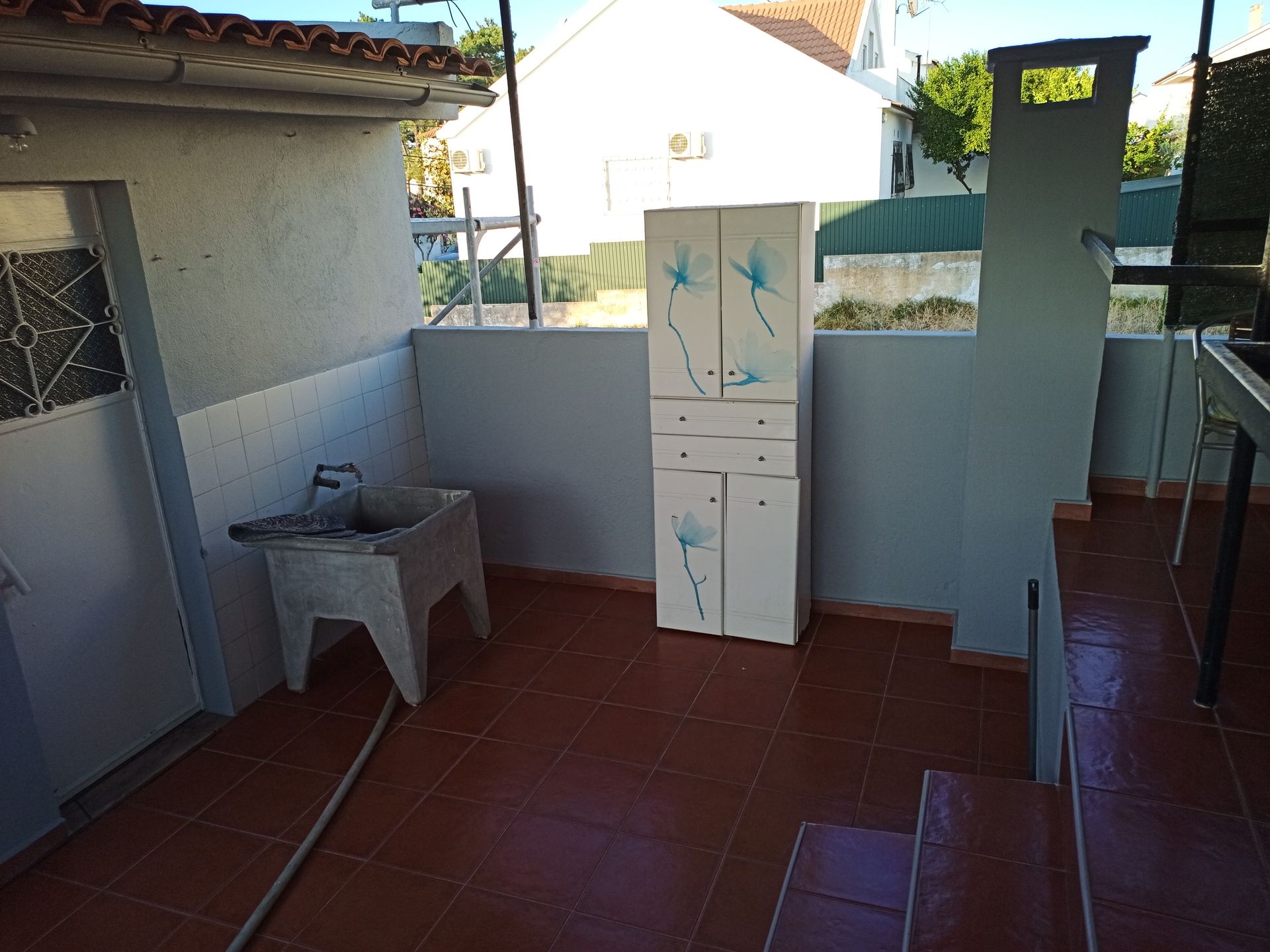 Pátio externo com armário branco, pia e degraus.