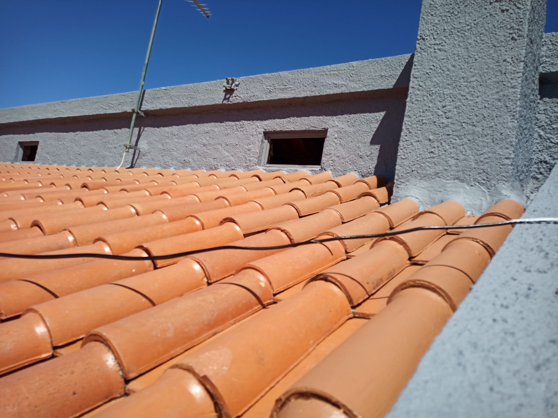 Telhado de telha laranja com edifício e chaminé em estuque cinza claro. Céu azul brilhante.