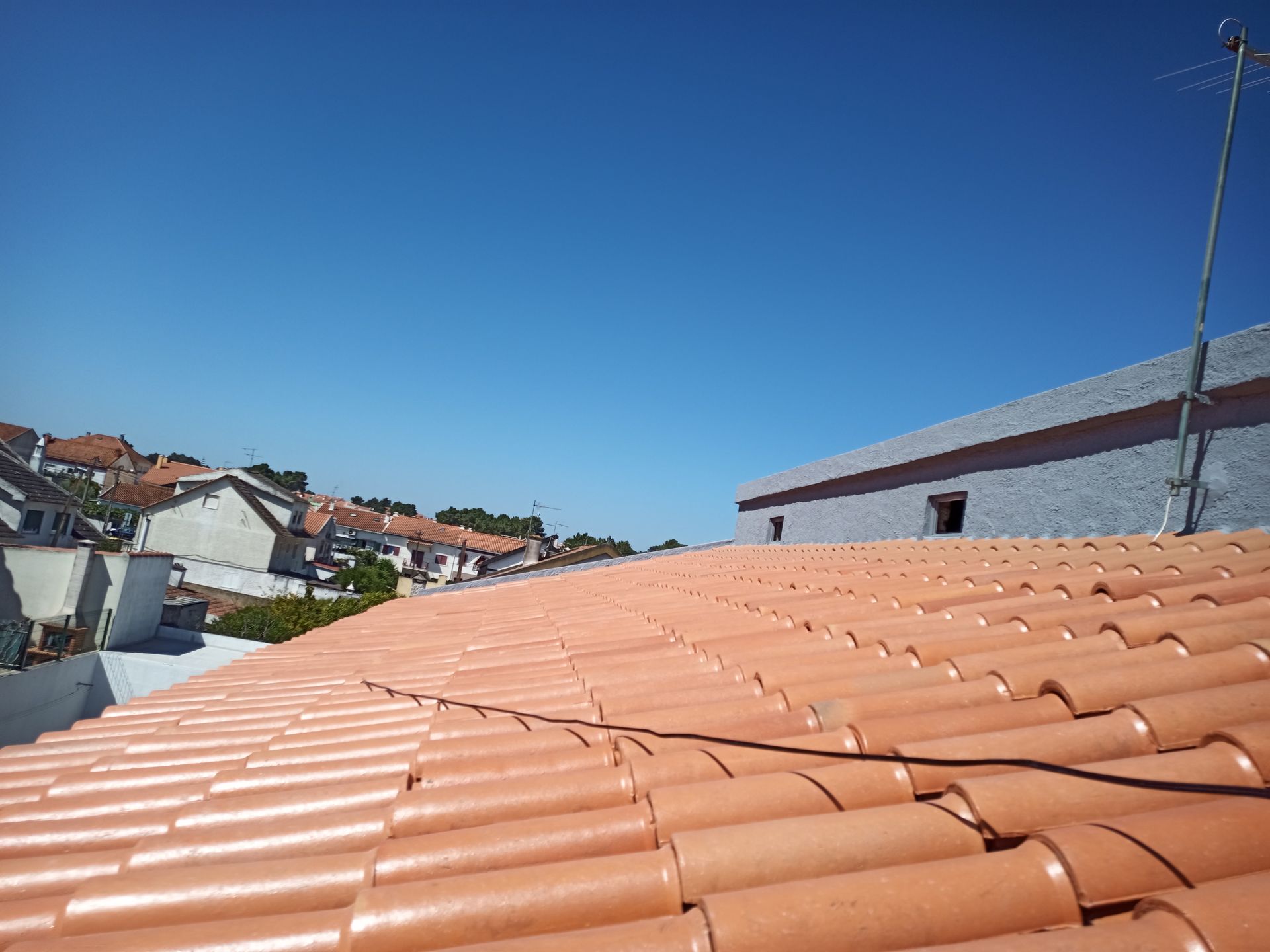 Telhado de telhas vermelhas com céu azul claro e prédios ao fundo.